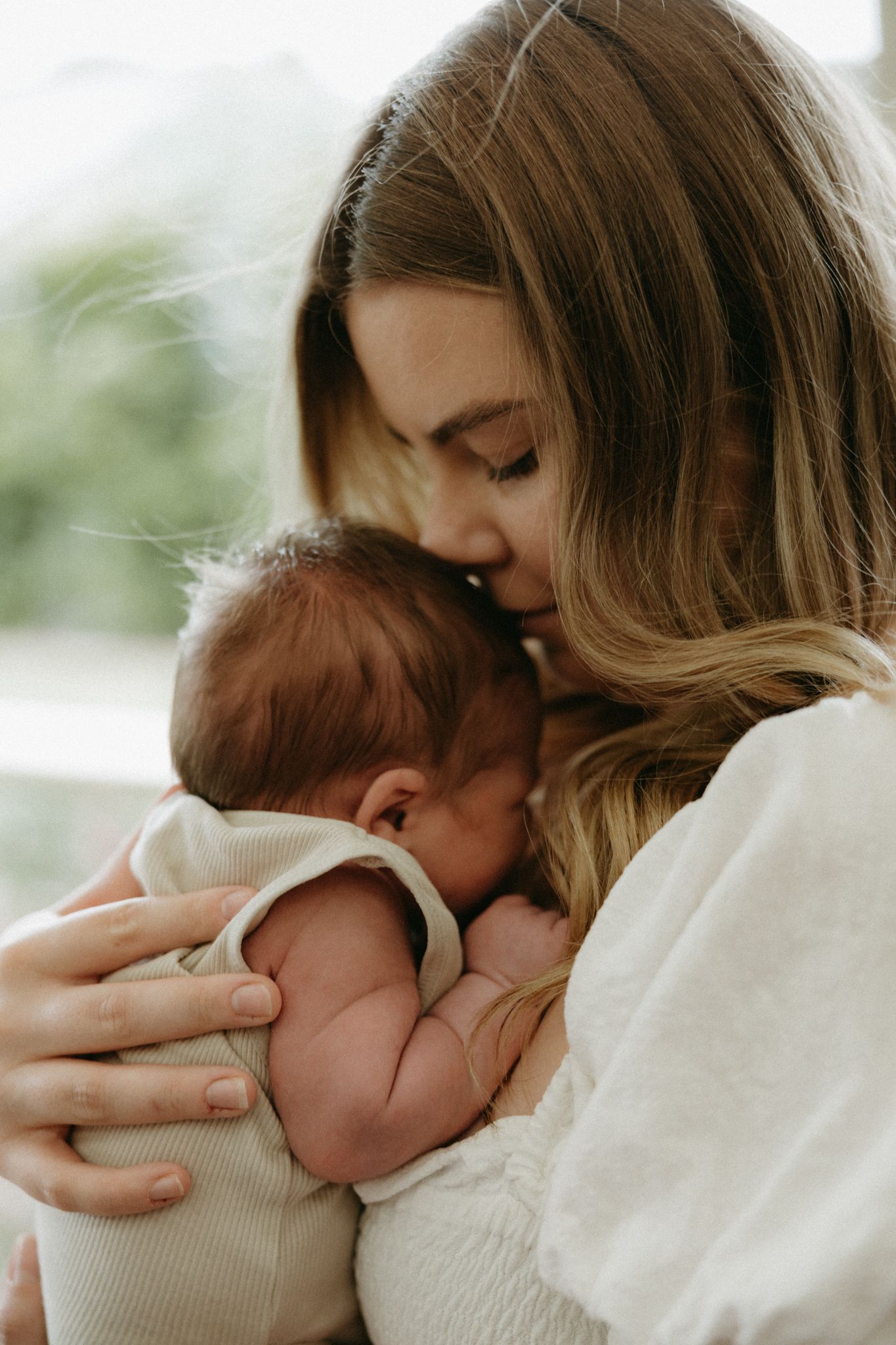 A tender moment as a young mother gently kisses her newborn baby, cradling the infant close in her arms.