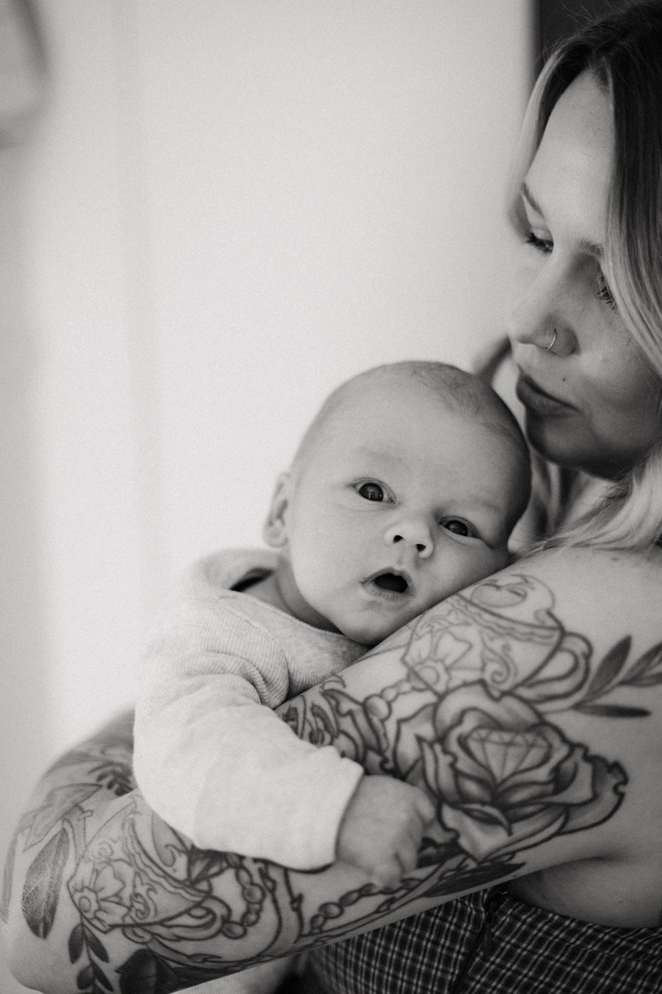 Black and white photo of tattooed mother tenderly holding her newborn baby close to her chest.