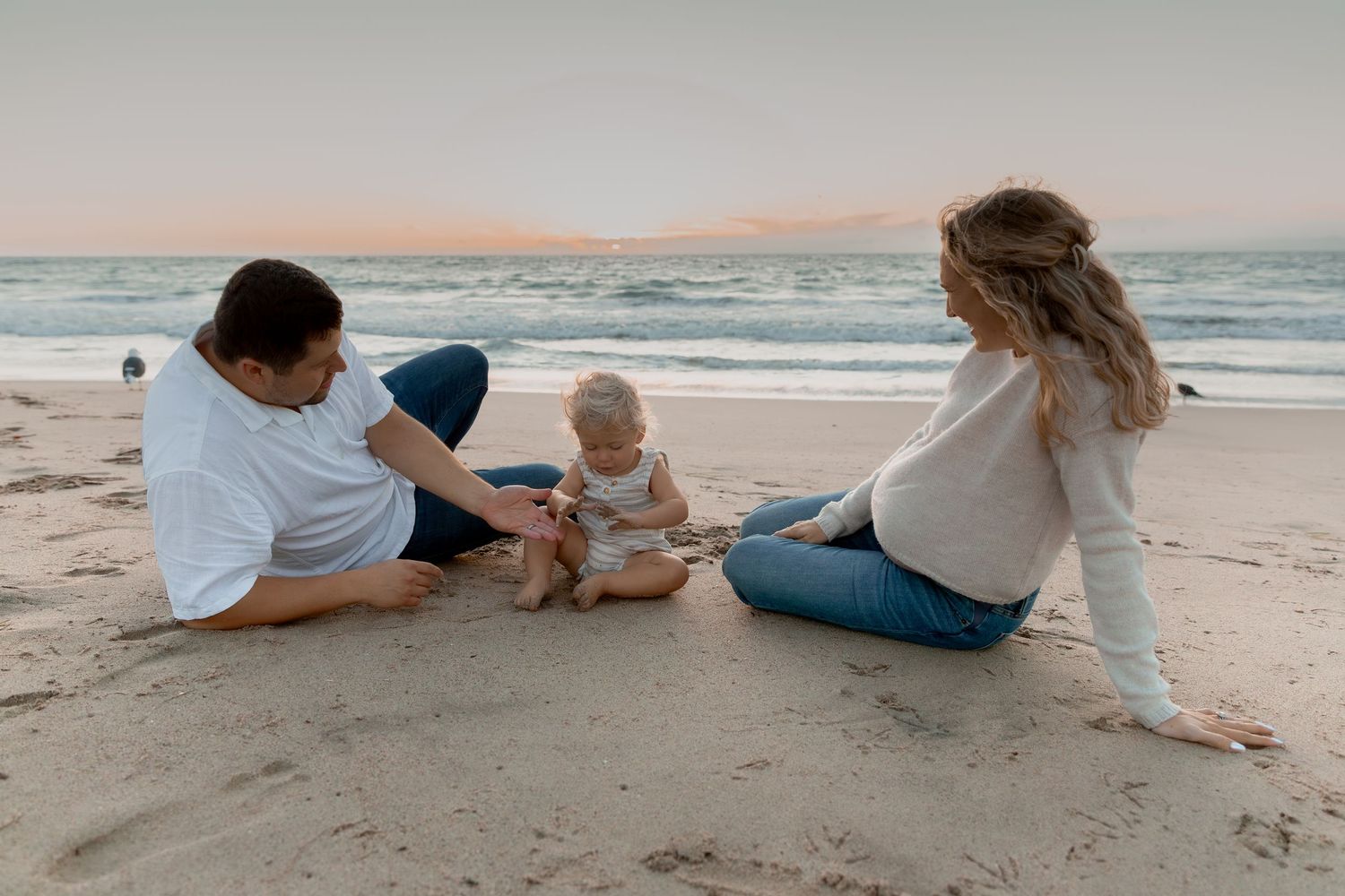 Family relaxing together on sandy beach during golden hour.