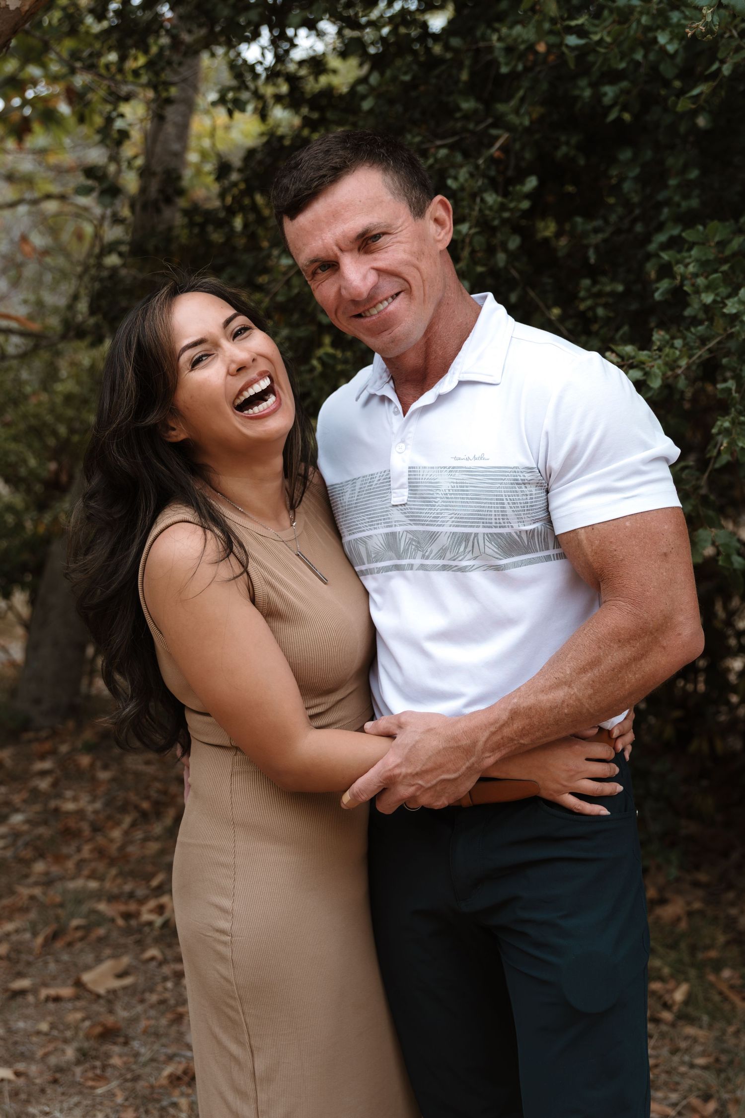 Playful couple sharing laughs and embraces in a wooded outdoor photoshoot.