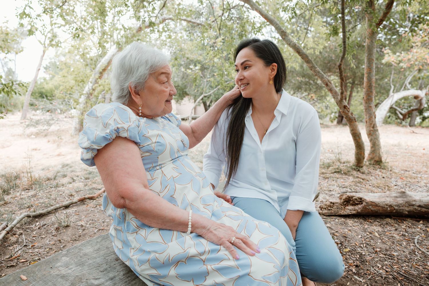 Two people share a joyful moment while sitting together on a log in a sunlit wooded area.
