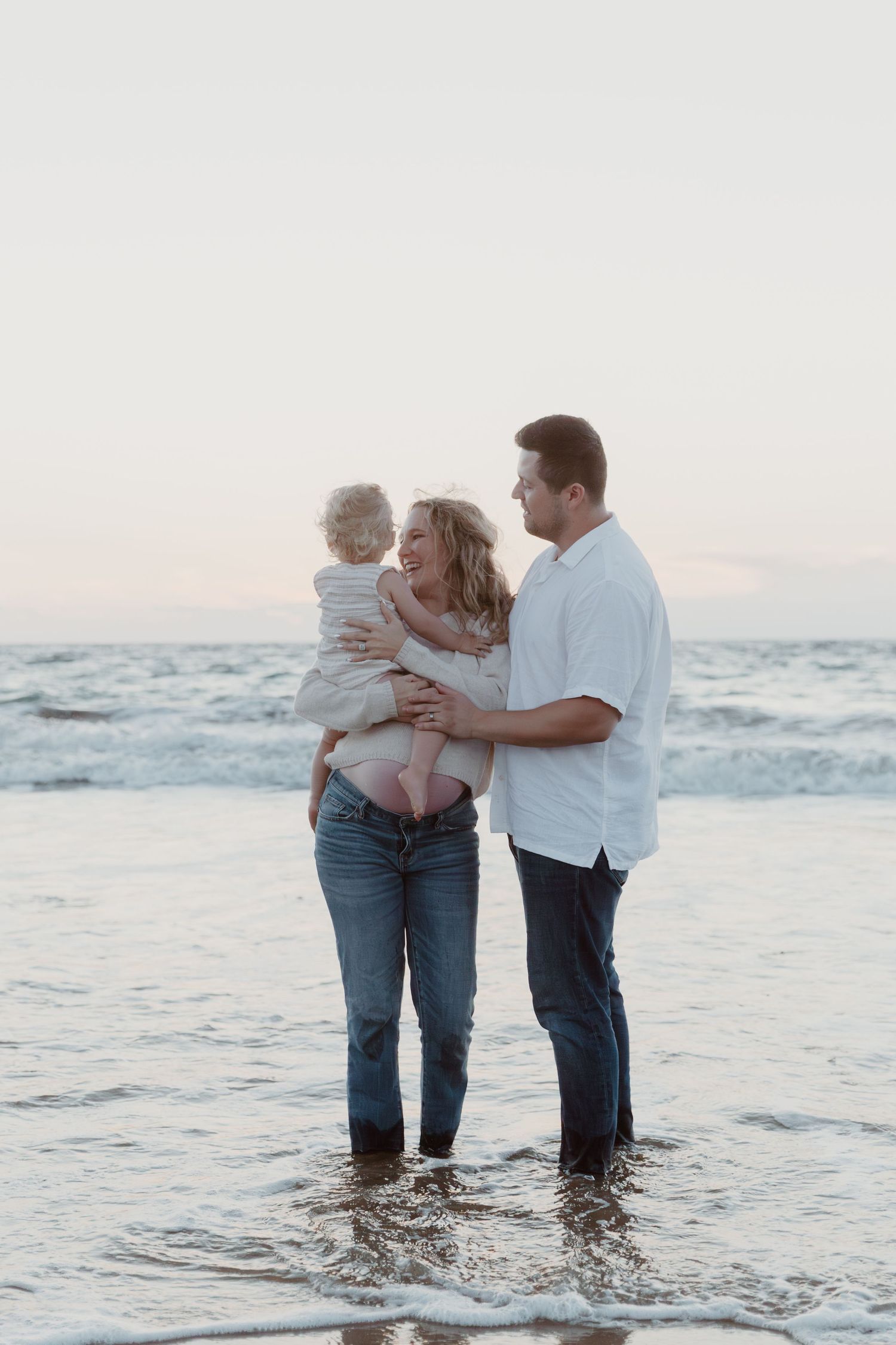 Family standing together in ocean waves at sunset creating precious beach memories.