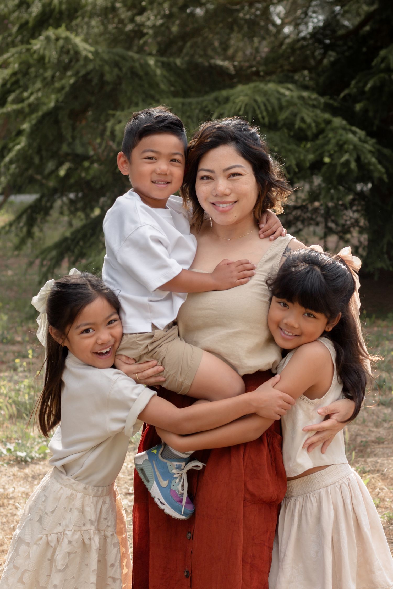 Family group hug captured in natural outdoor setting with pine trees in background.