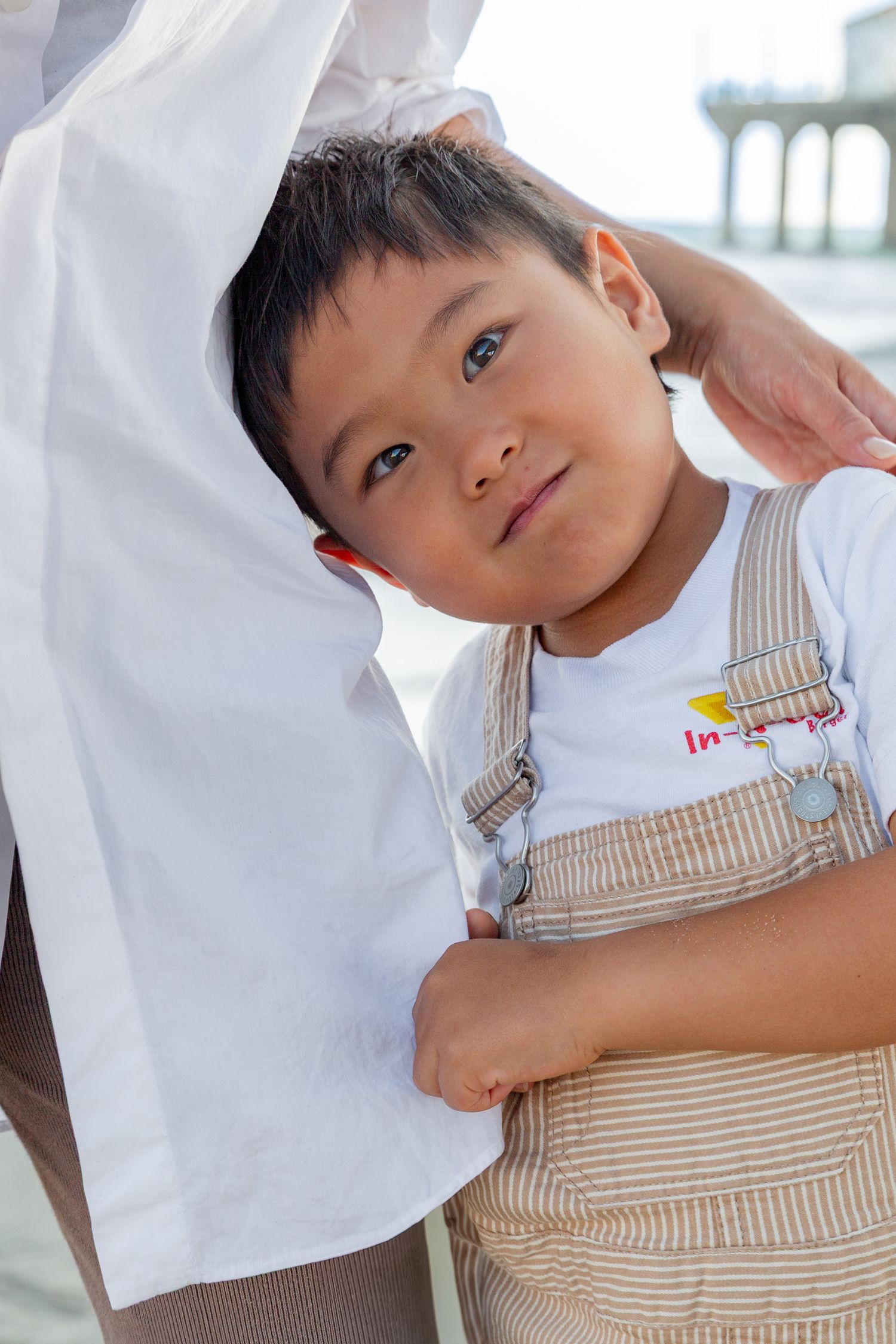 Young child in striped overalls plays and poses playfully against a white background.