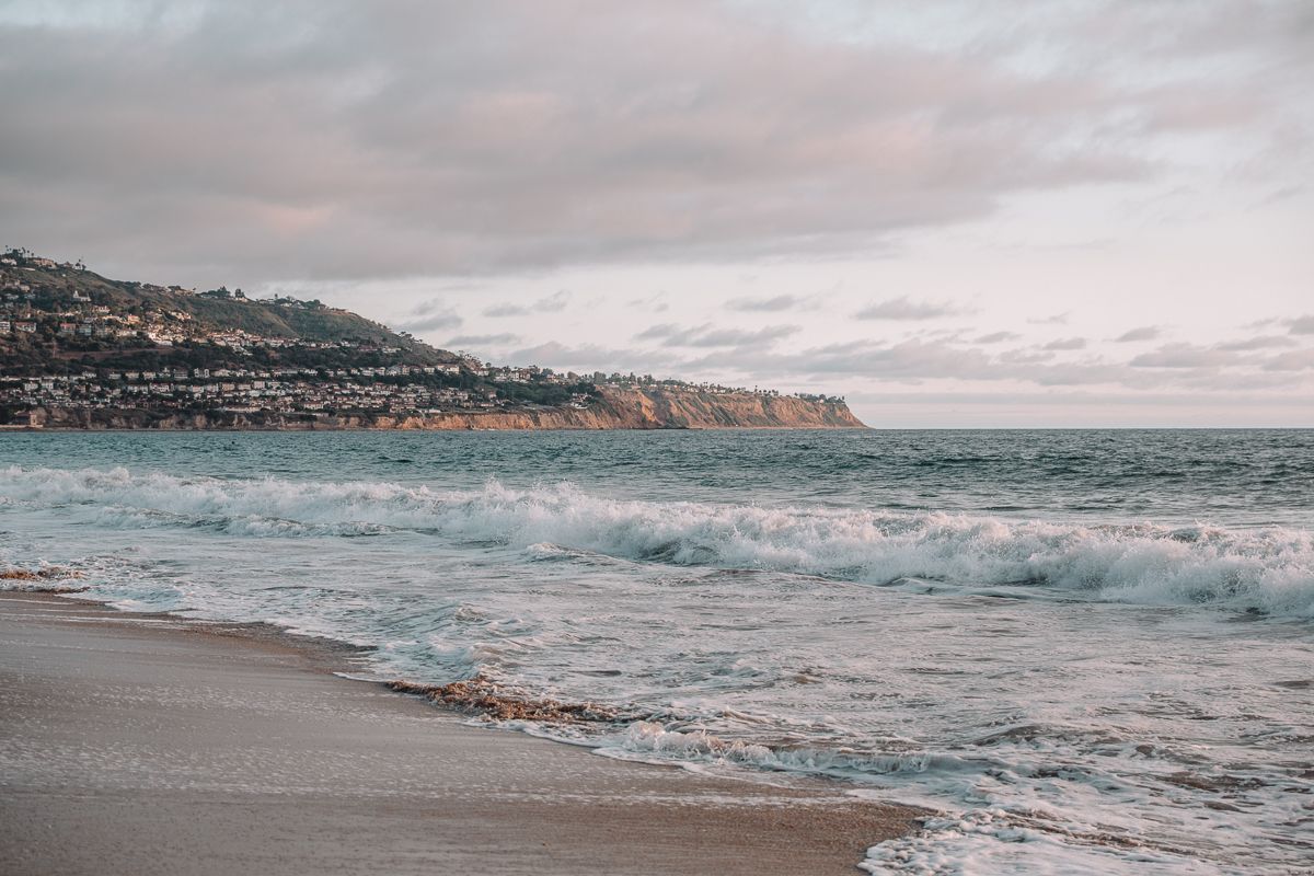 Dramatic coastal landscape with cliffs and rolling waves under an overcast sky.