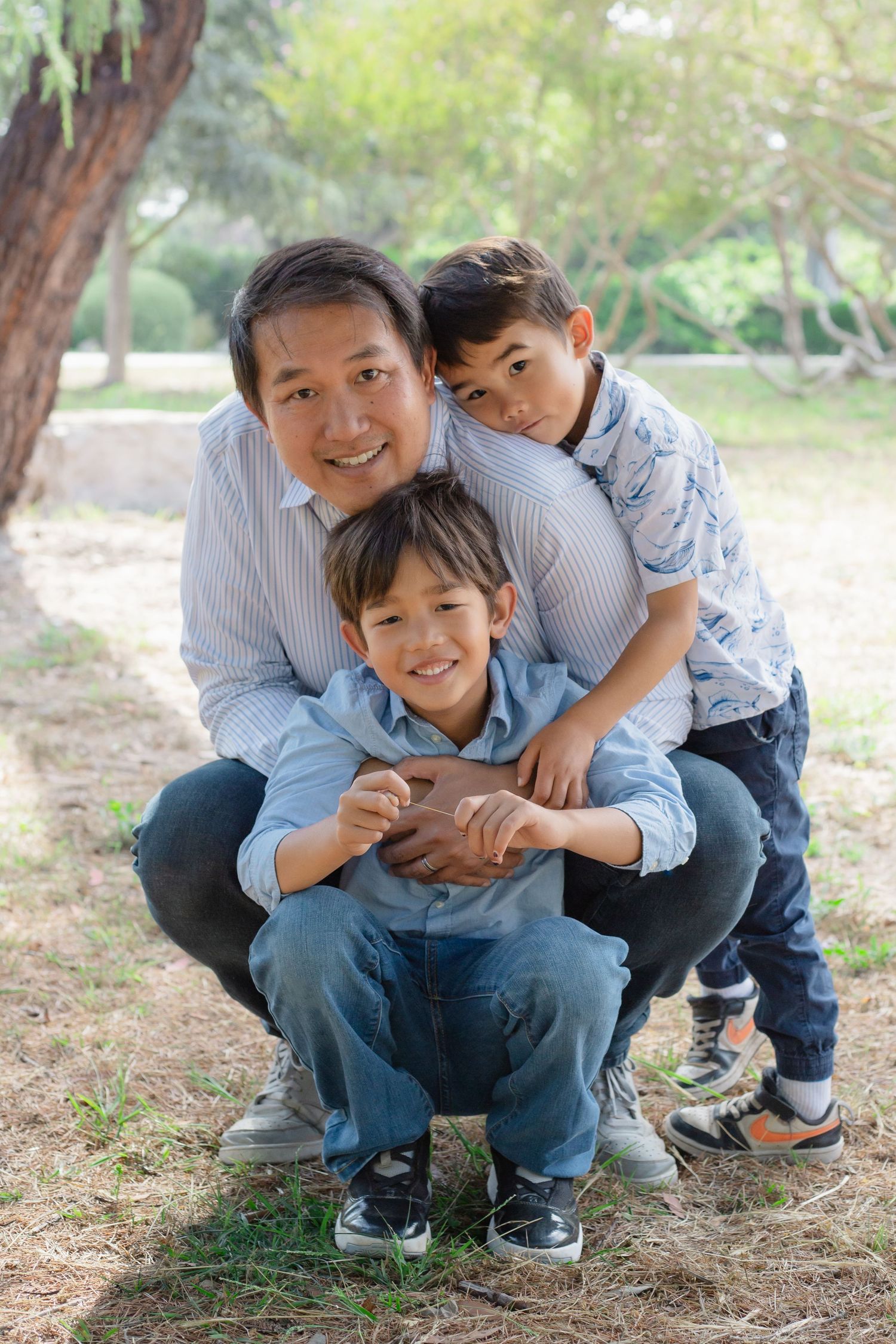Candid outdoor family photo shoot showing joyful interactions under trees.