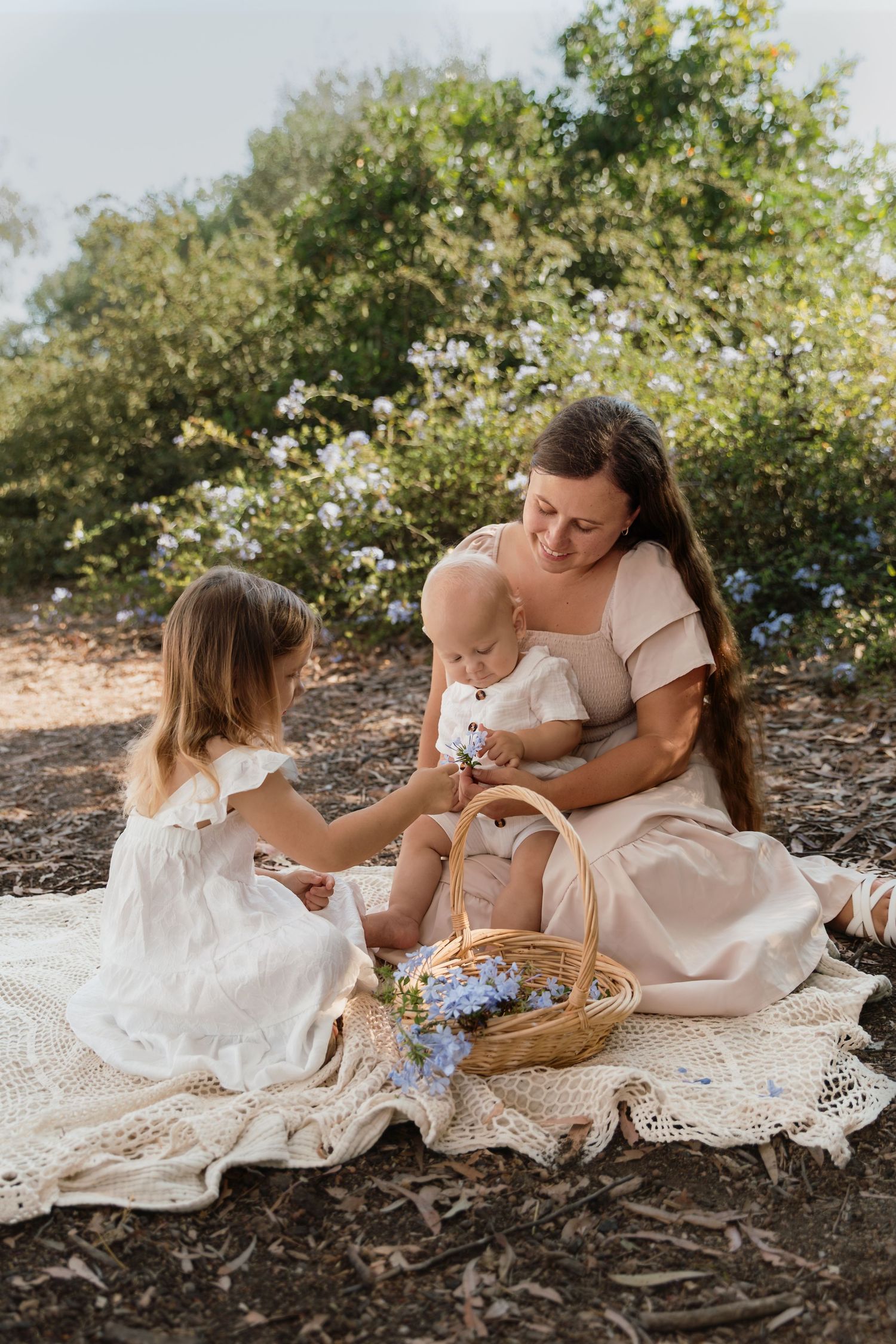 Family spending time together on white lace blanket with wicker basket in natural setting.