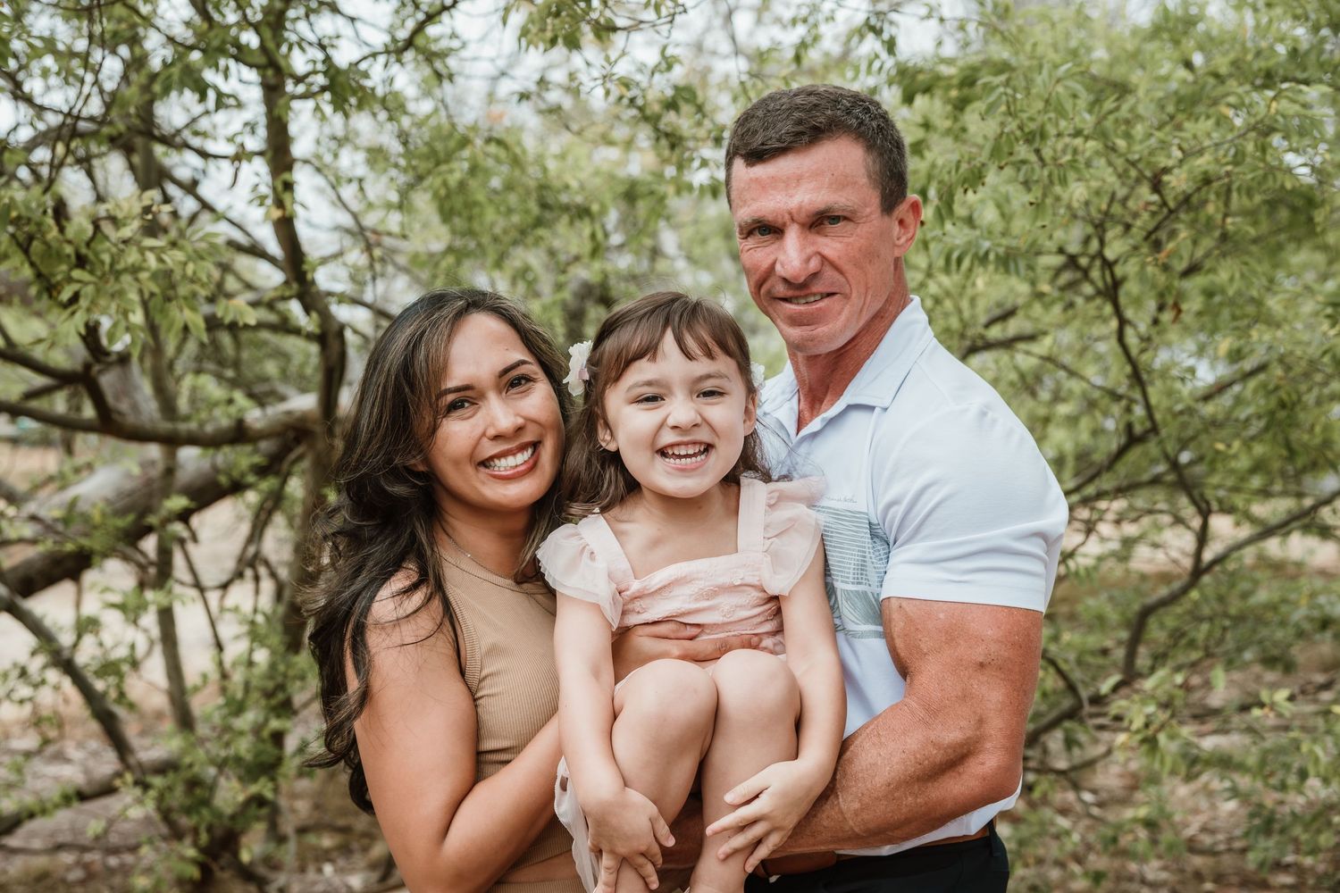 Family enjoying a playful moment together outdoors in a natural setting with green trees in the background.