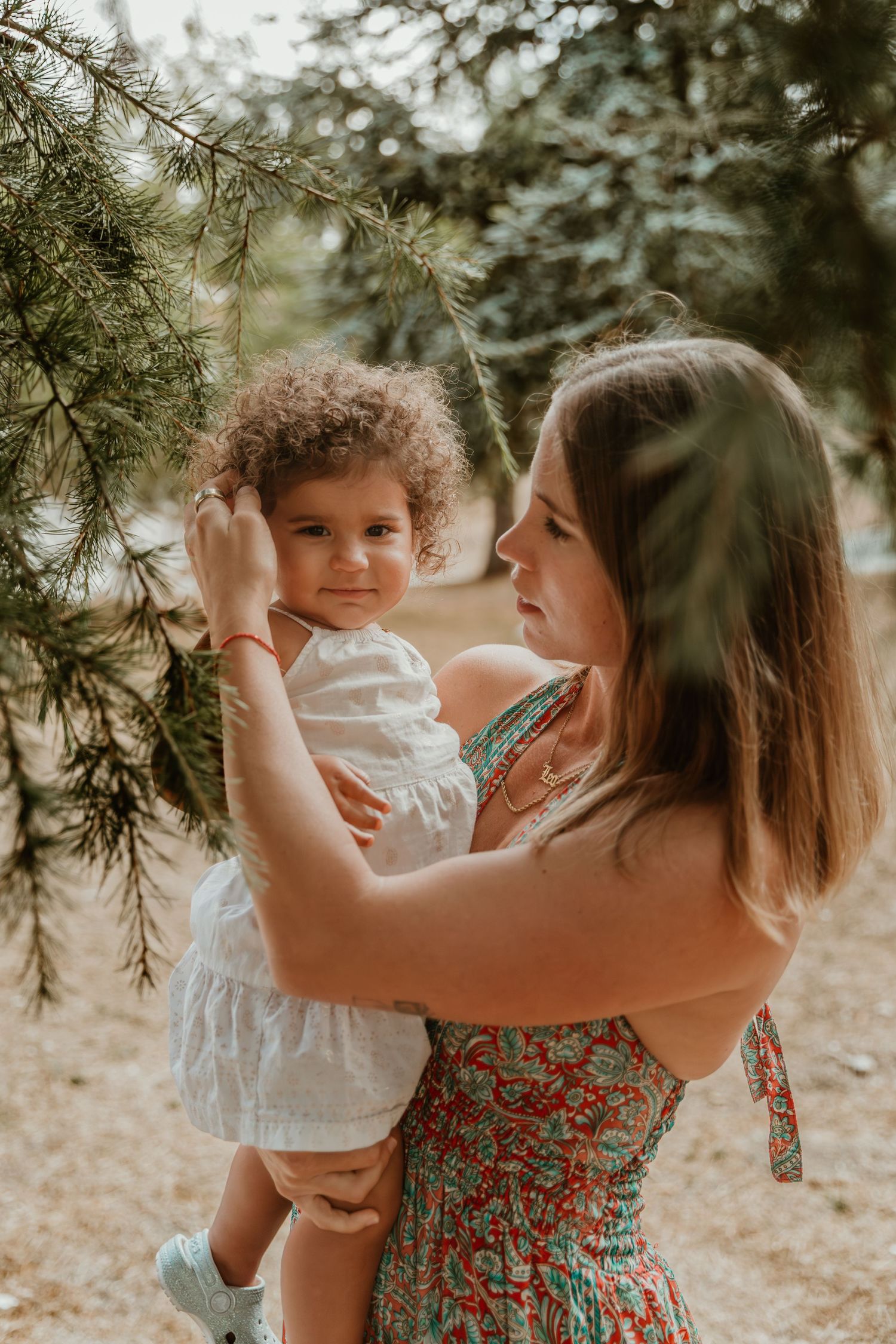Parent and child sharing tender moment under pine trees in outdoor setting.