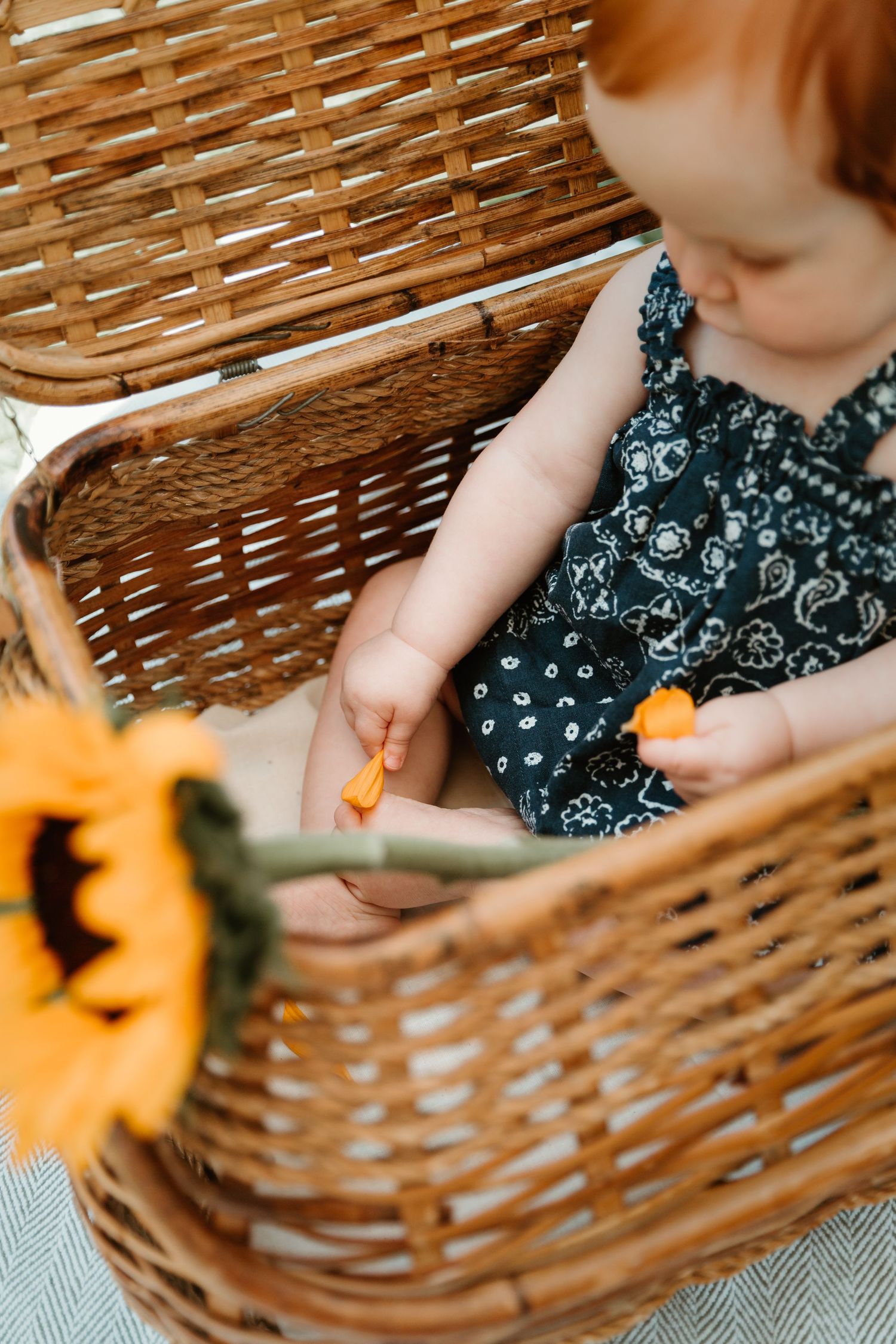 A woven basket with sunflowers sits beside someone in a floral dress.