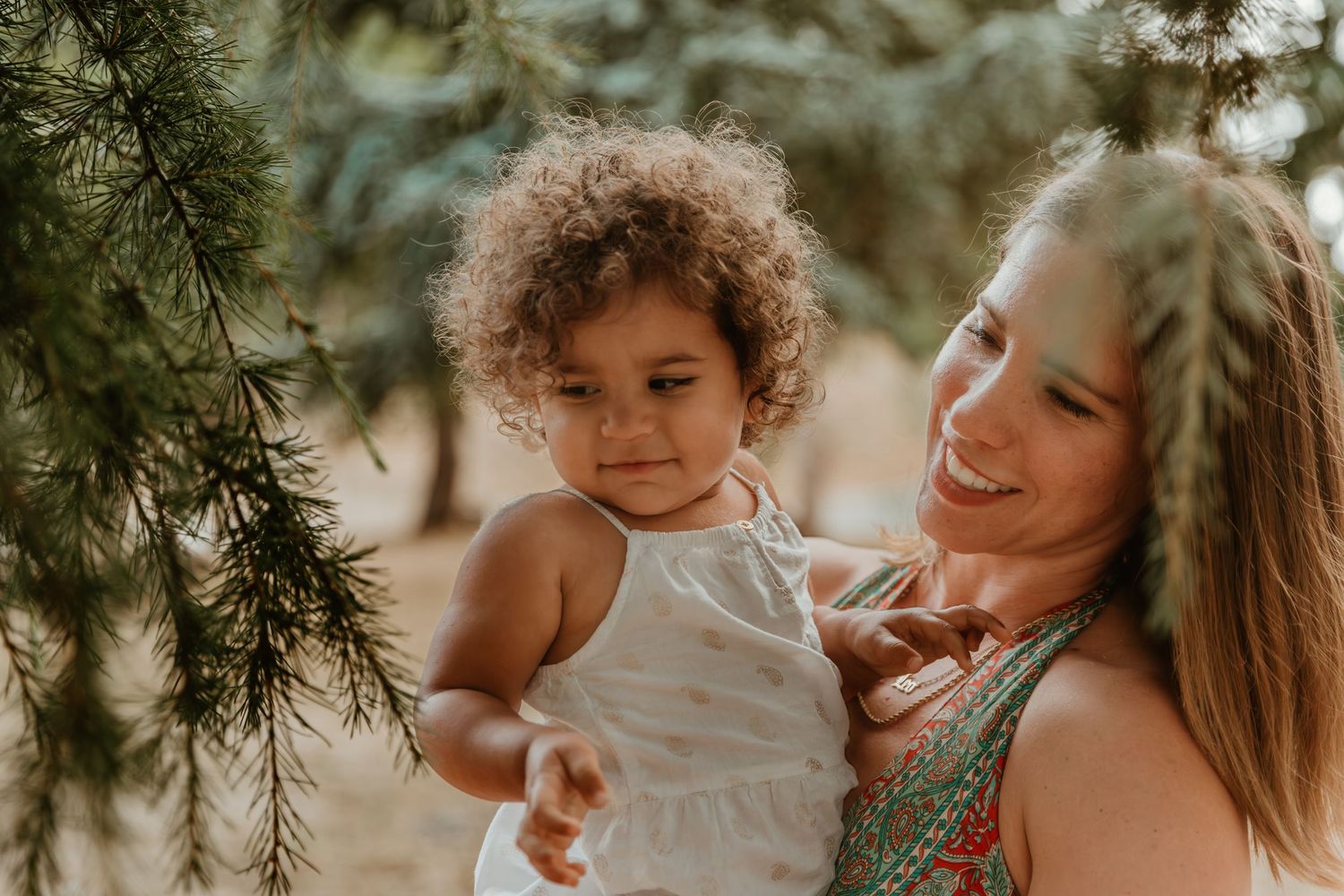 A tender moment captured under pine trees in warm golden light.