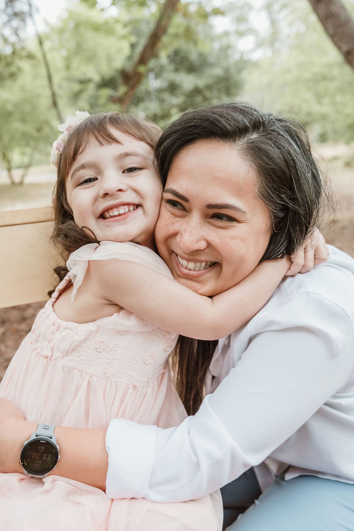 A joyful embrace between two people in a pink dress and white shirt sitting outdoors on a sunny day.