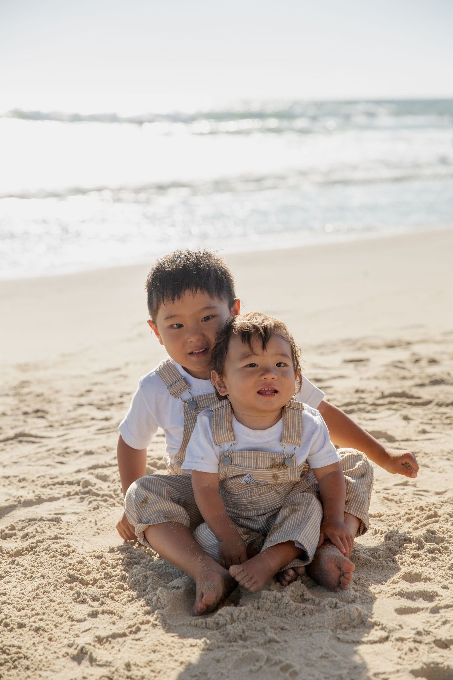 Two young children in matching outfits playing together on a sunny beach.