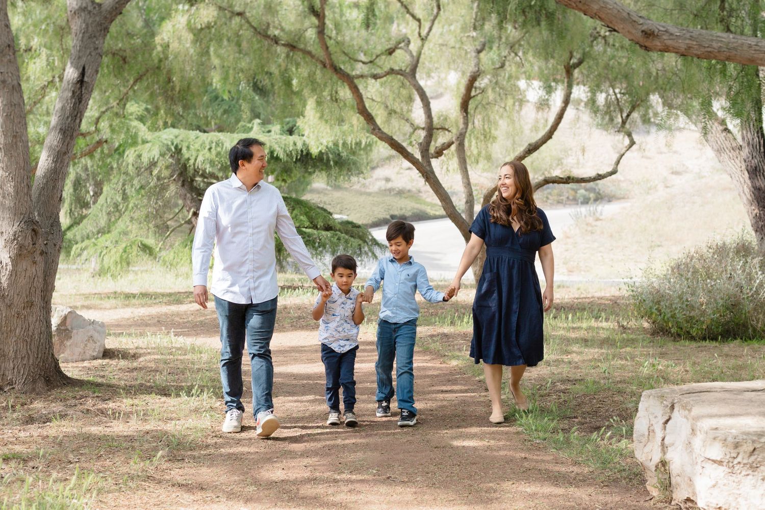 Wide landscape shot of family walking together under tree-lined path.