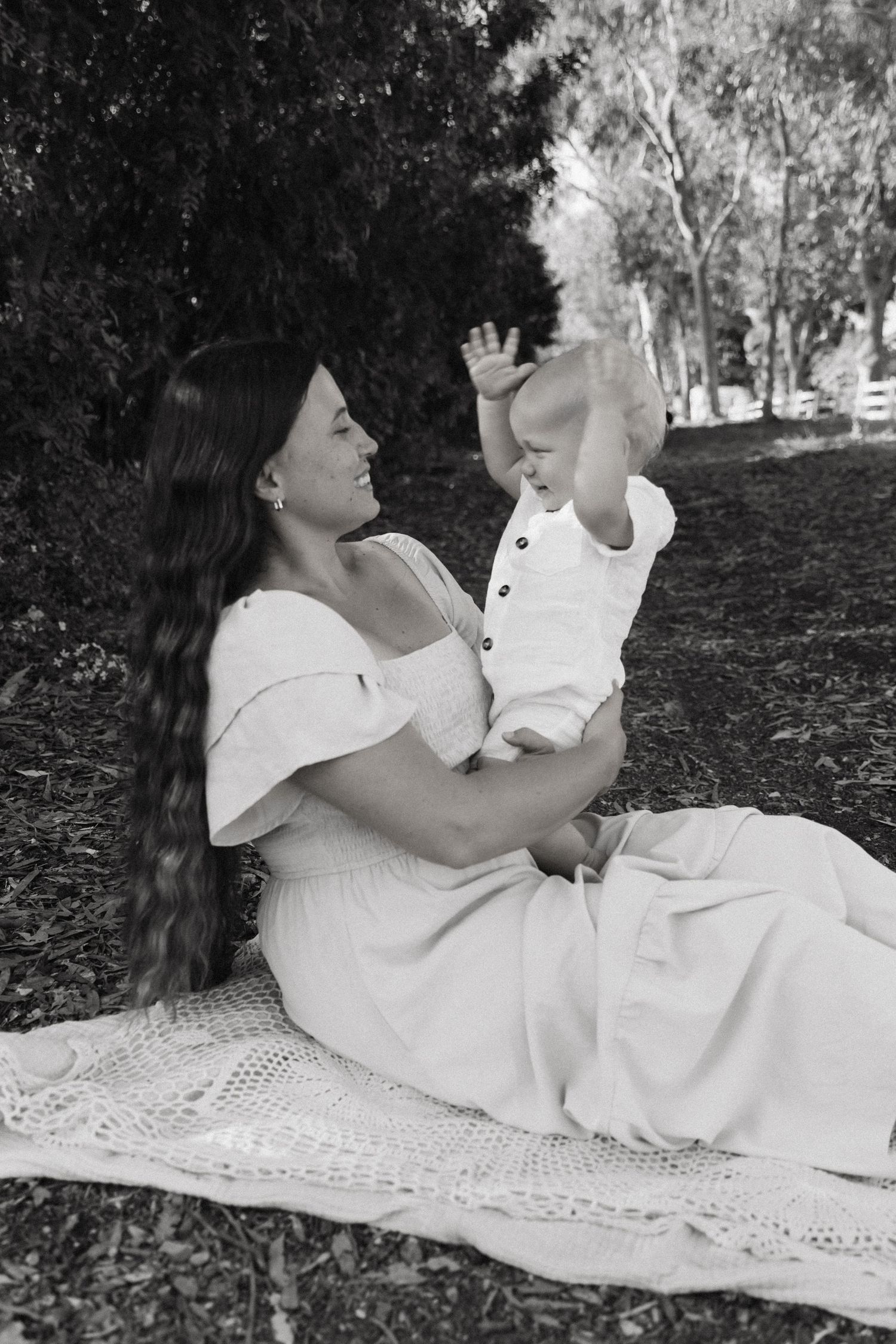 Black and white photo of people in white dresses relaxing on a lace blanket outdoors.