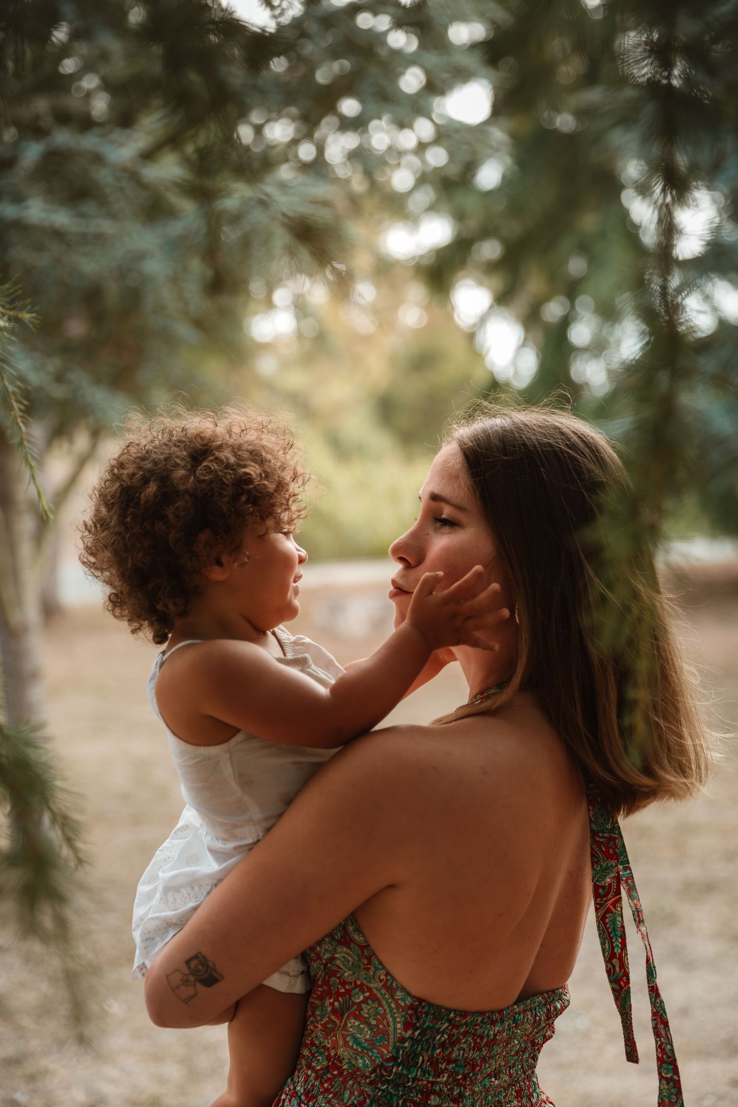 Parent and child sharing affectionate moment under evergreen trees at sunset.