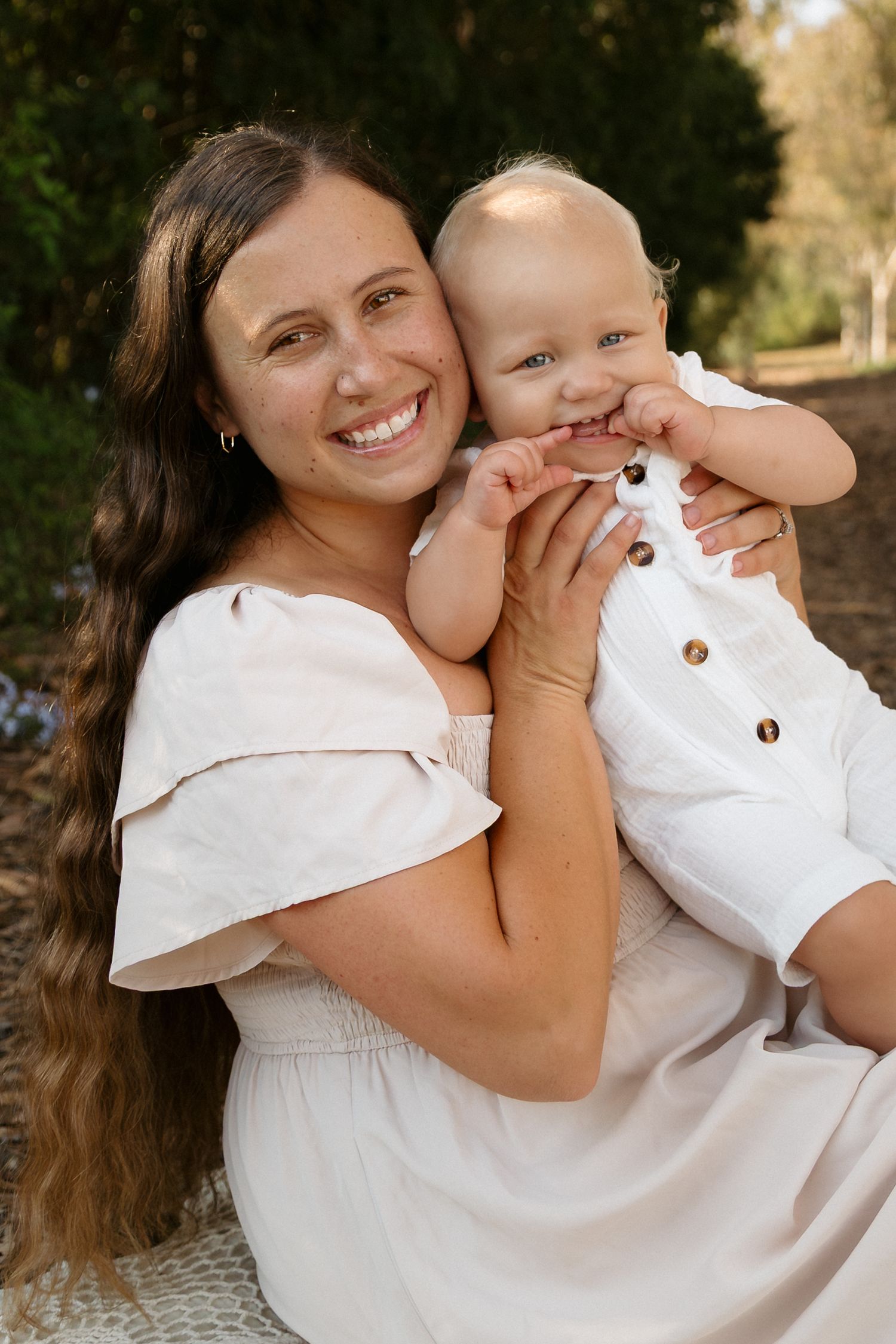 Joyful outdoor portrait session in white outfits against natural backdrop.