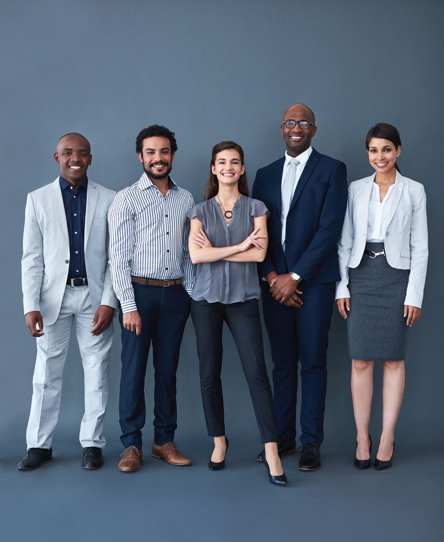 Five diverse business professionals posing confidently together against a dark gray studio background.