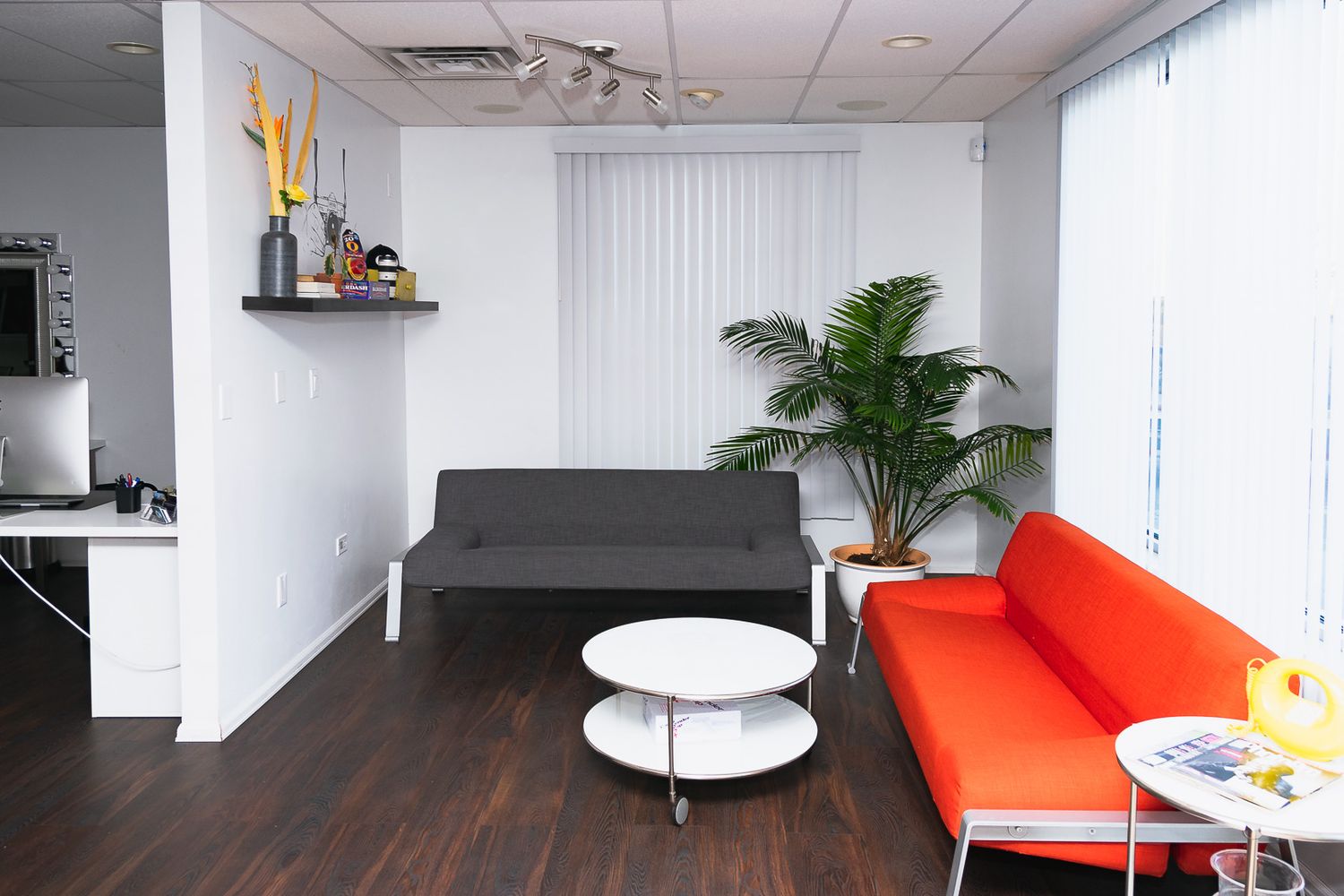 Modern office interior with white walls, dark hardwood floors, and vibrant orange furniture accents.