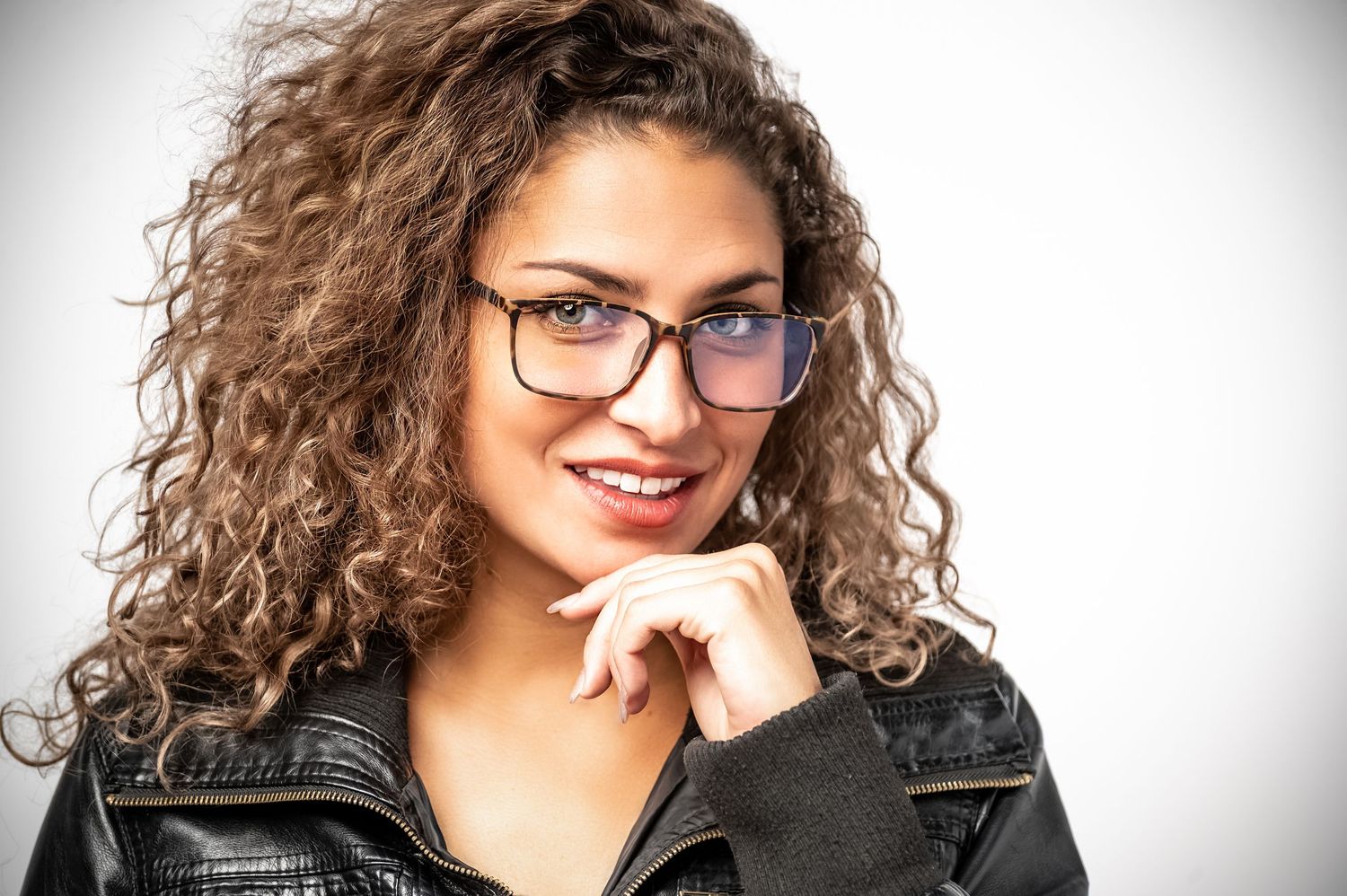A person with curly brown hair and glasses smiles while wearing a black leather jacket in a series of expressive poses.