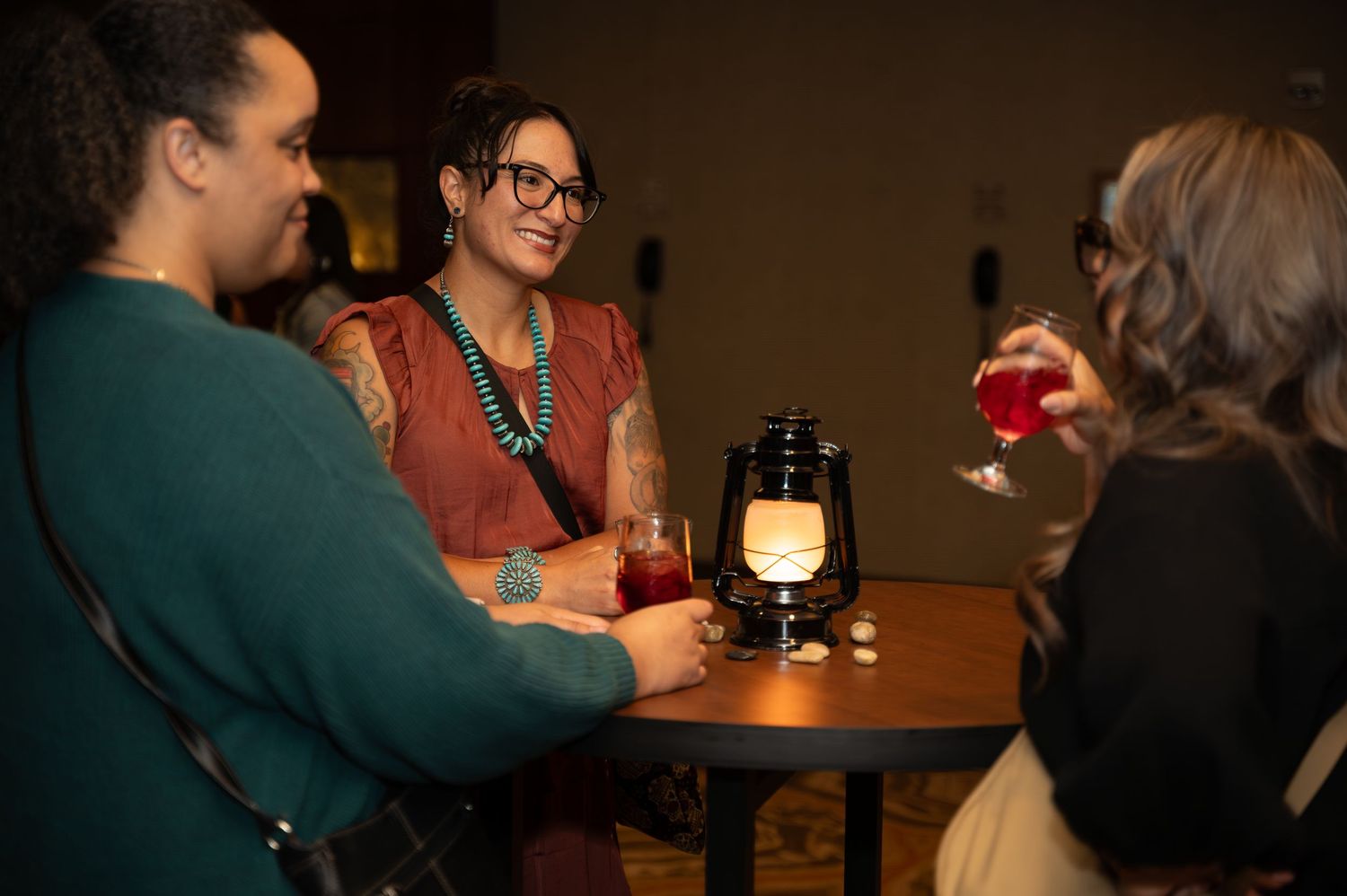 People gather at a dimly lit table with lanterns creating an intimate atmosphere for drinks and conversation.