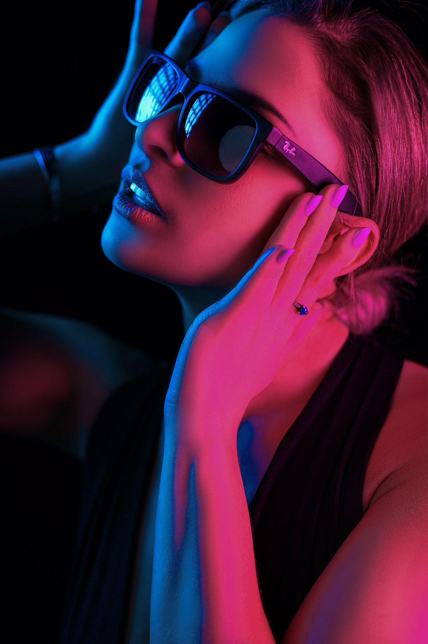 Woman wearing Ray-Ban sunglasses posed under dramatic blue and pink neon lighting against a dark background.