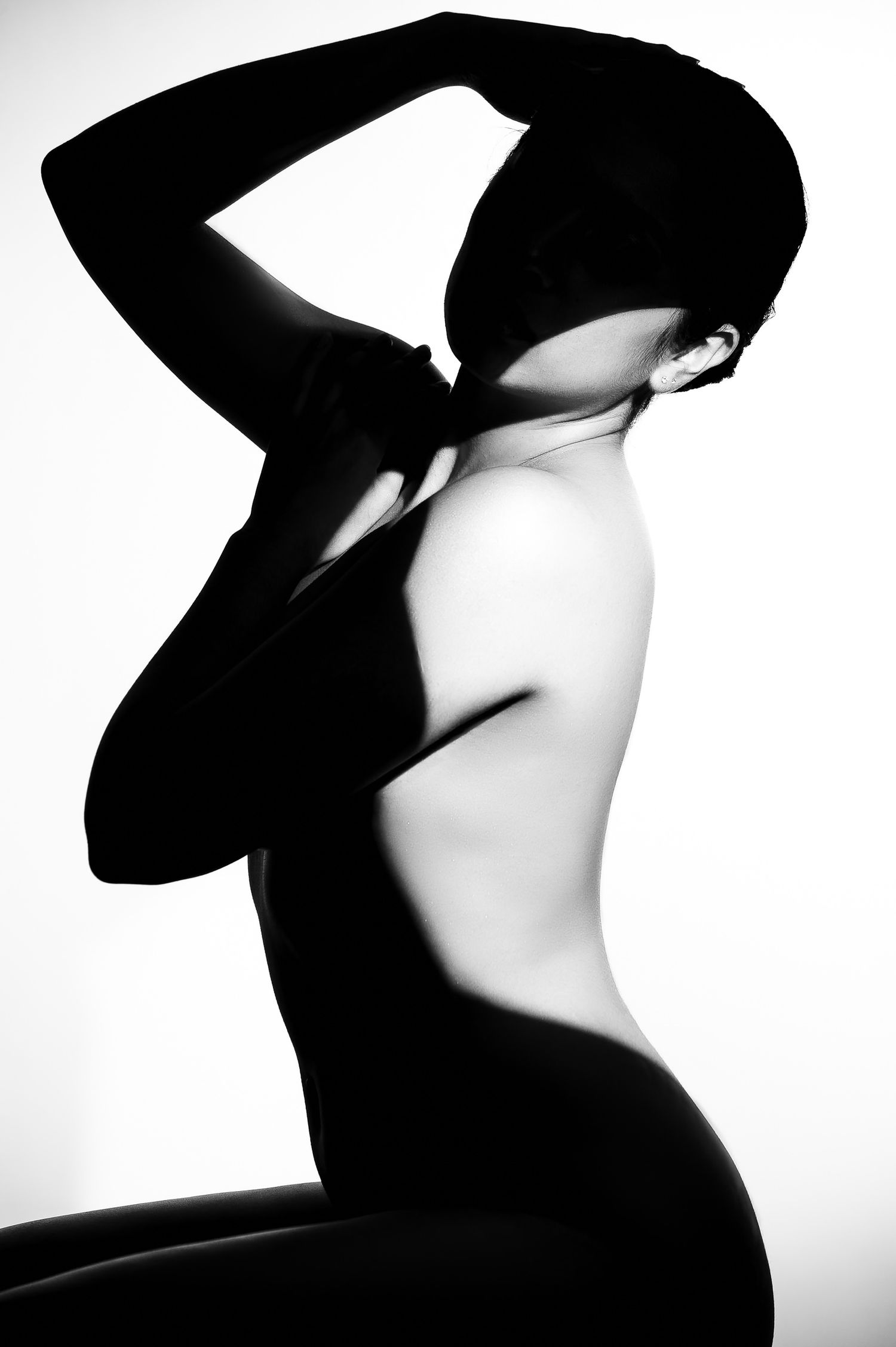 Black and white artistic nude photography featuring dramatic shadows on a woman's back against a white background.