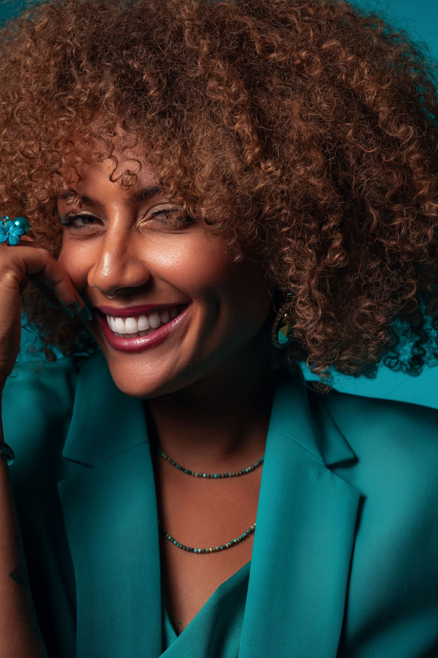 Vibrant portrait featuring natural curly hair and teal blazer against dark background.
