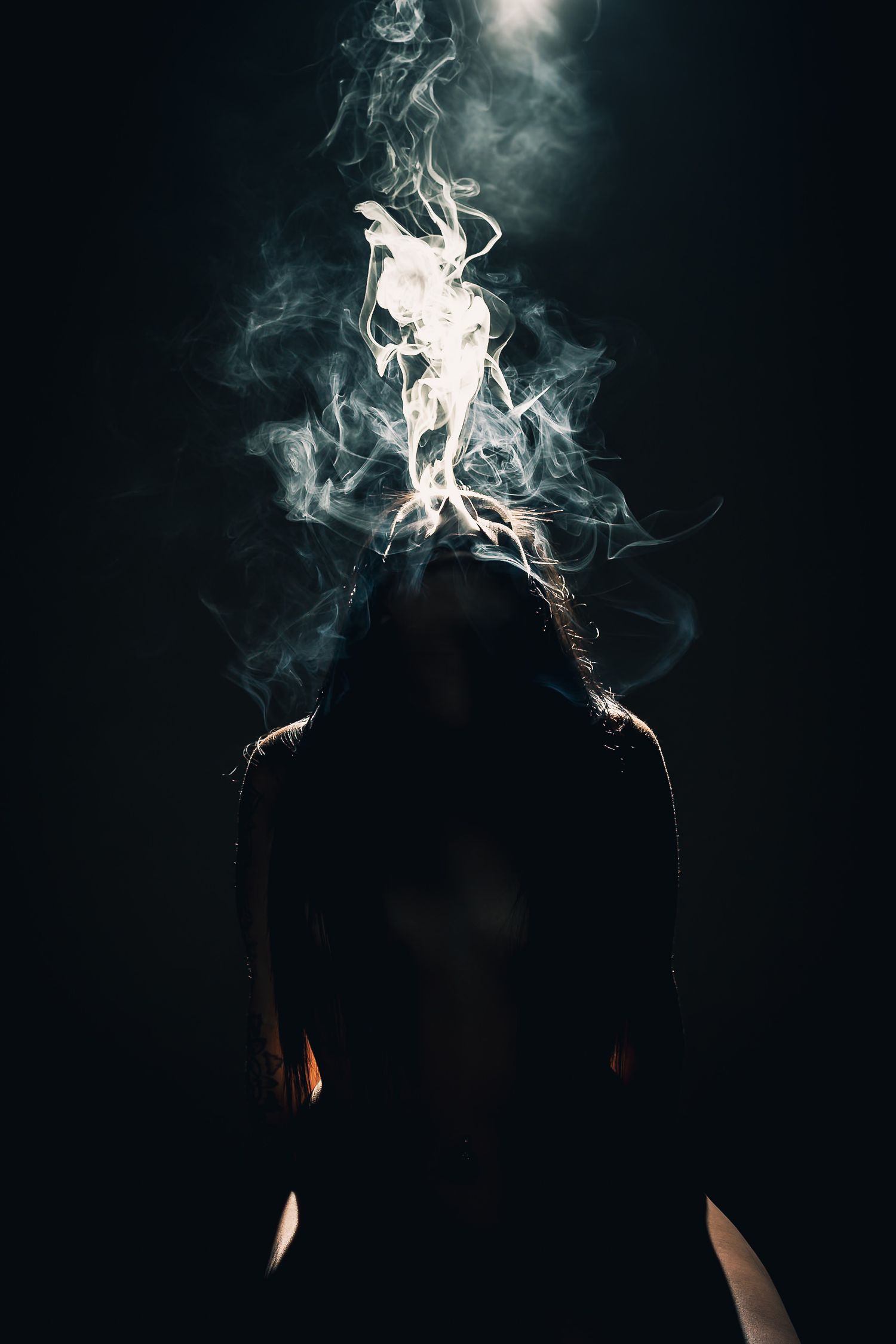 Mysterious silhouette of a person with dramatic white smoke swirling above their head against a dark background.