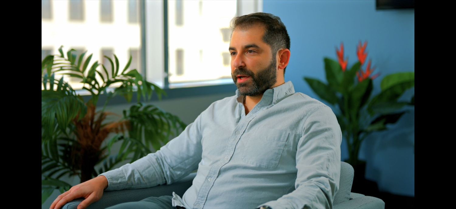 Person in light blue shirt sitting in modern office space with indoor plants and natural lighting.