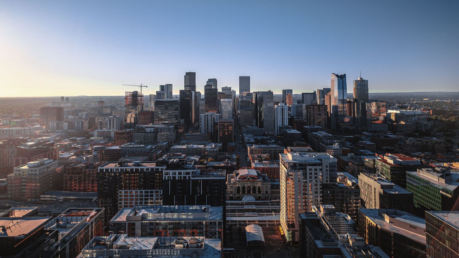 Panoramic aerial view of a city skyline with modern buildings and streets stretching across the horizon at sunset.