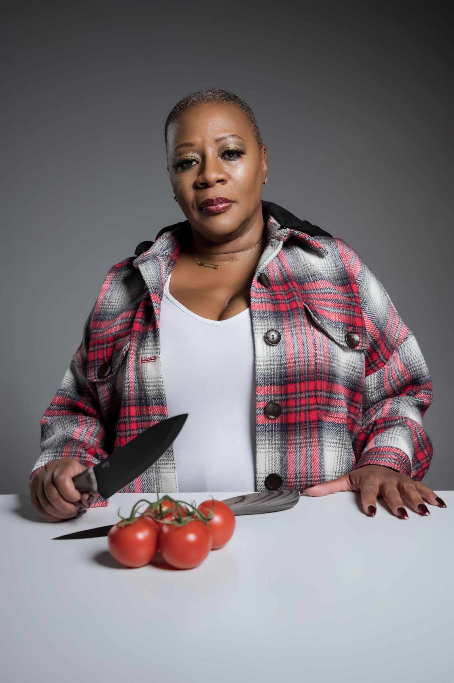 A person in a plaid flannel jacket sits at a white table with fresh red tomatoes in a creative portrait series.