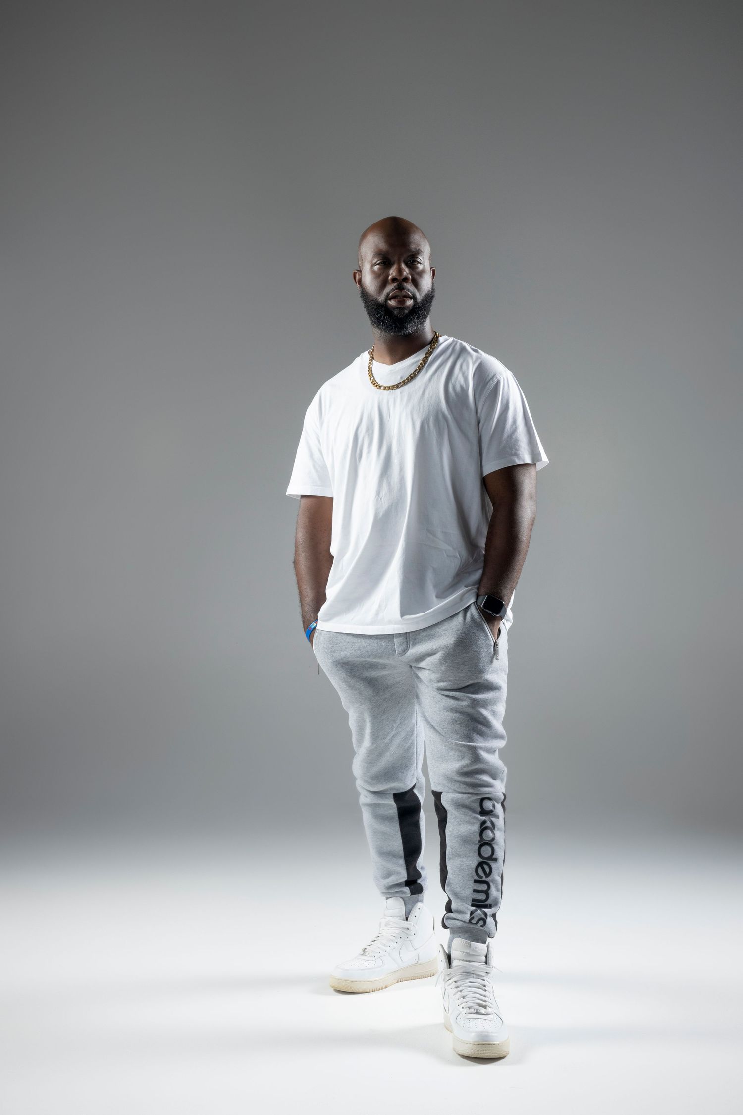 A person in an all-white outfit with white sneakers poses against a gray studio background in different positions.