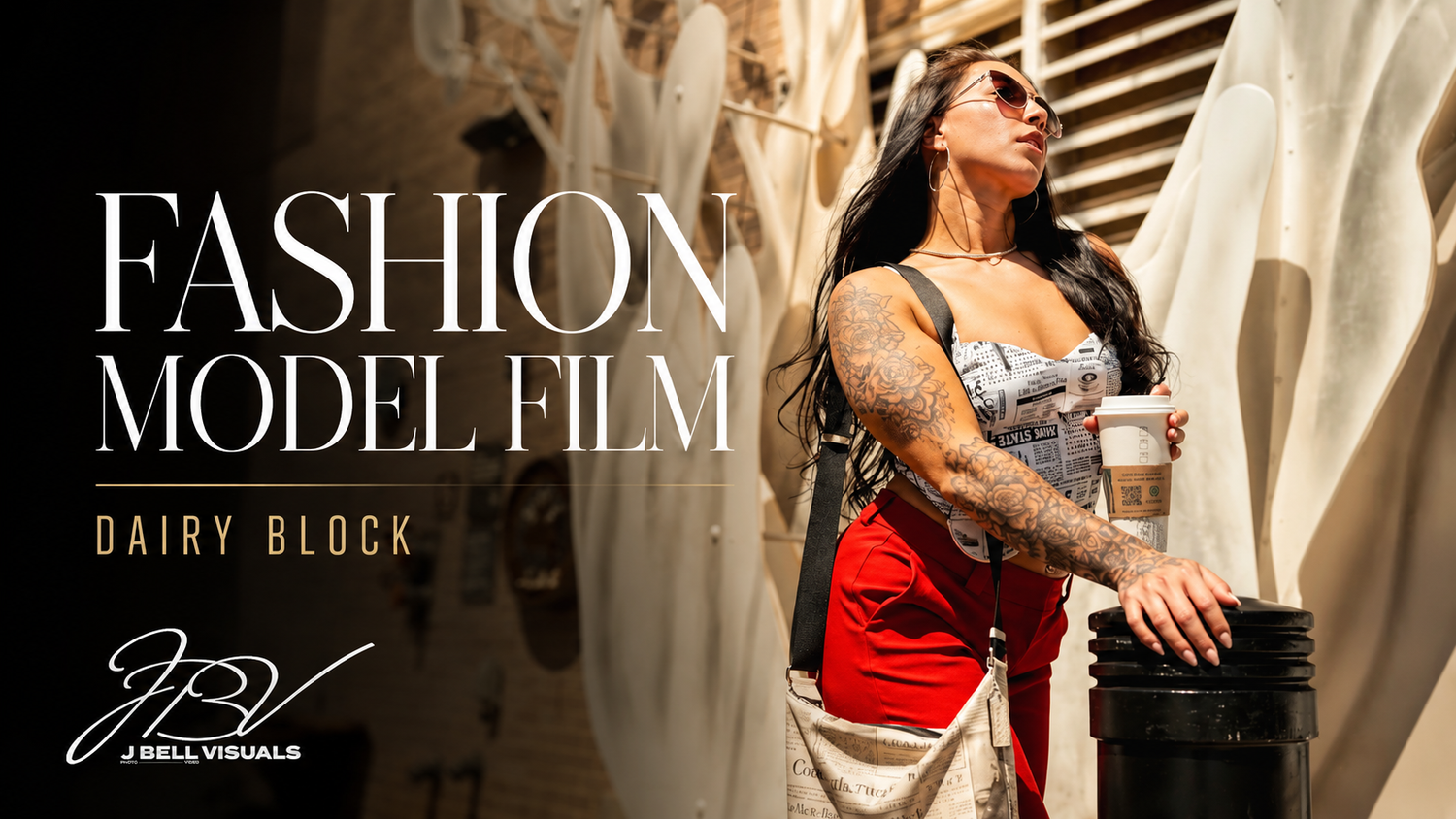 Tattooed female fashion model poses outdoors at Dairy Block, wearing red pants and denim top, holding a coffee cup.