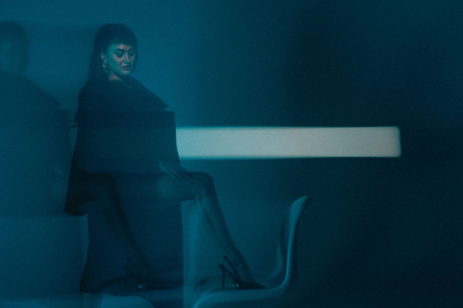 Person sitting at a white table in dramatic teal-blue lighting against a dark moody background.