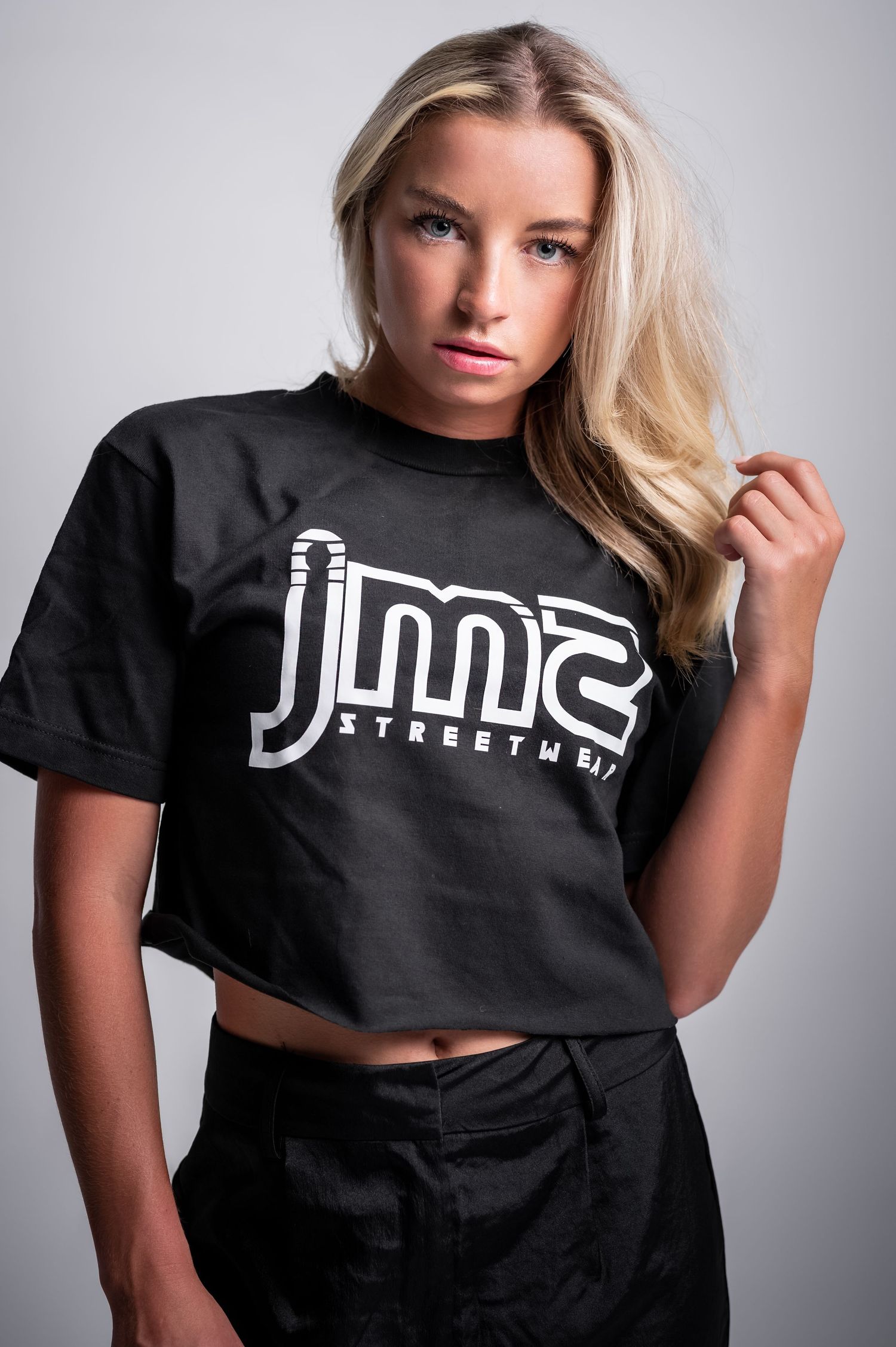 Model wearing black crop top with white text logo in series of poses against gray studio backdrop.