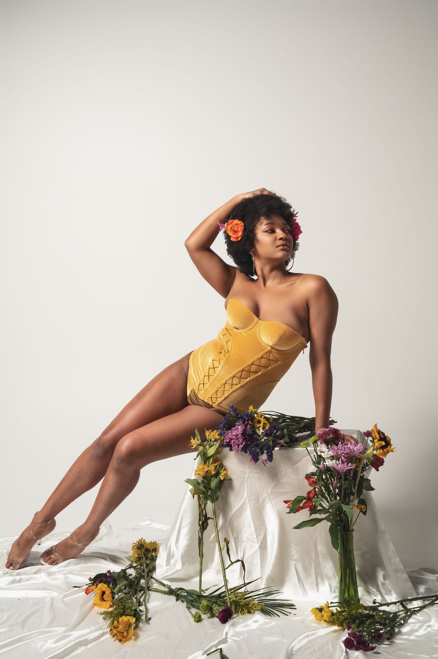 Artistic studio shoot with floral arrangements and yellow dress creating elegant poses on white background.