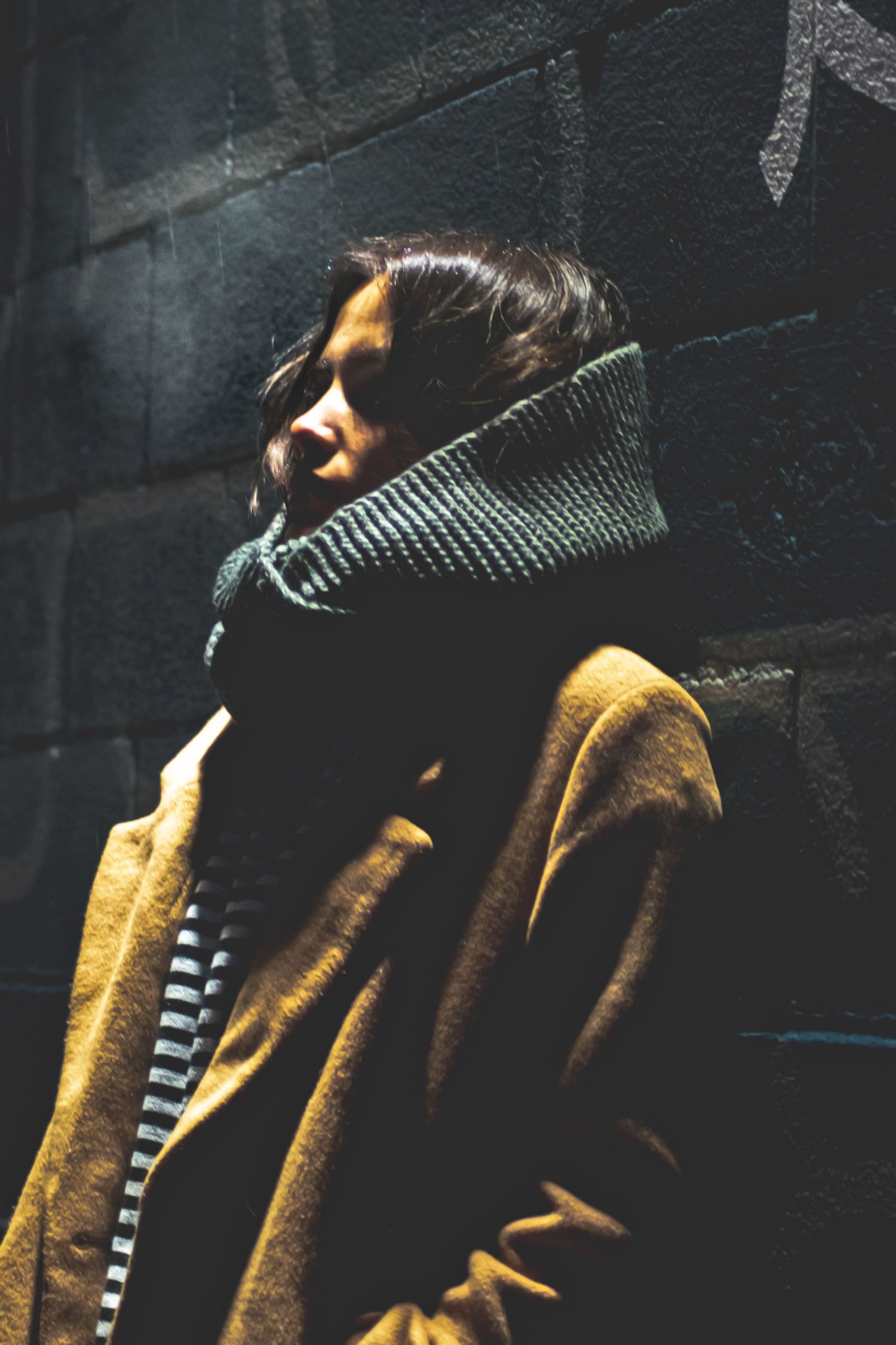 Dramatic side view of person wearing striped and brown sweaters in moody dark lighting with shadows.