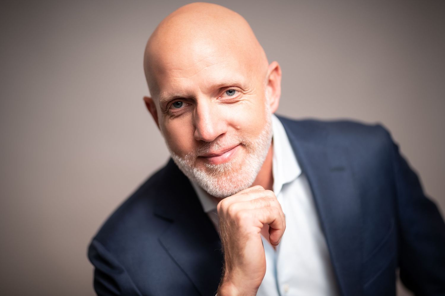 Professional headshot series in navy suit and white shirt against neutral background.