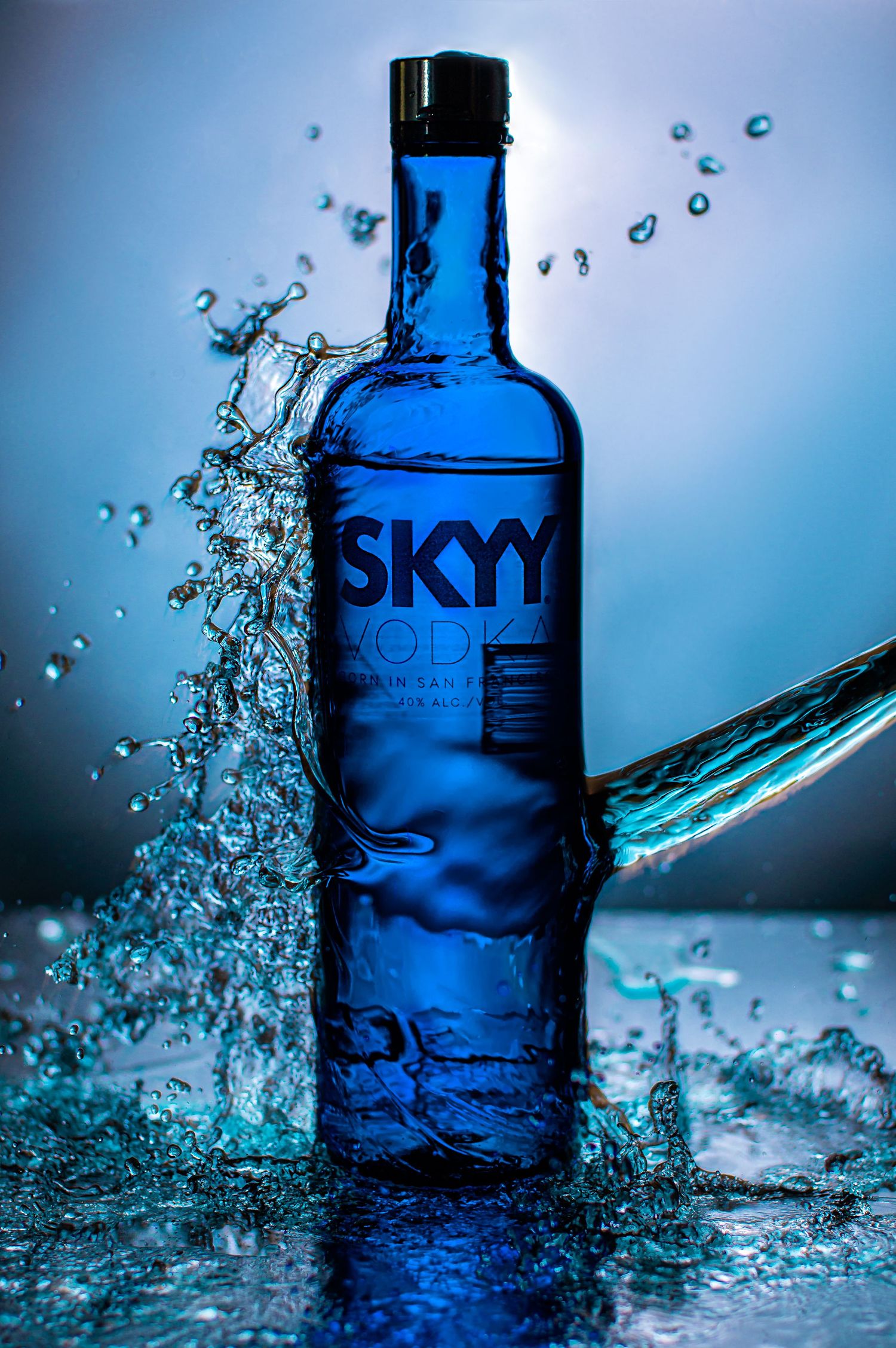 SKYY vodka bottle with dynamic water splashes against blue background creating artistic liquid motion photography.