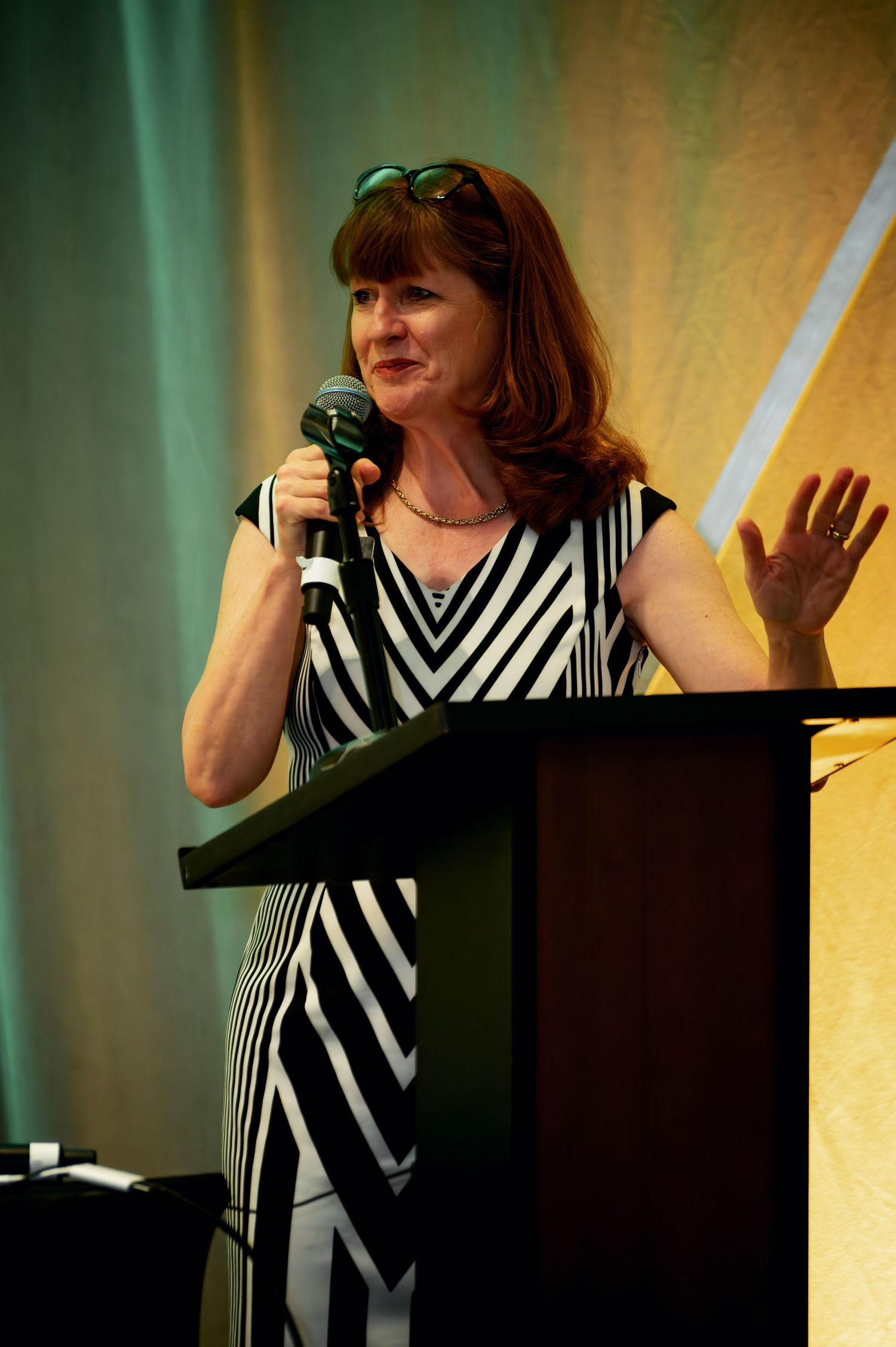 A speaker in a black and white striped dress gestures while presenting at a podium on stage.