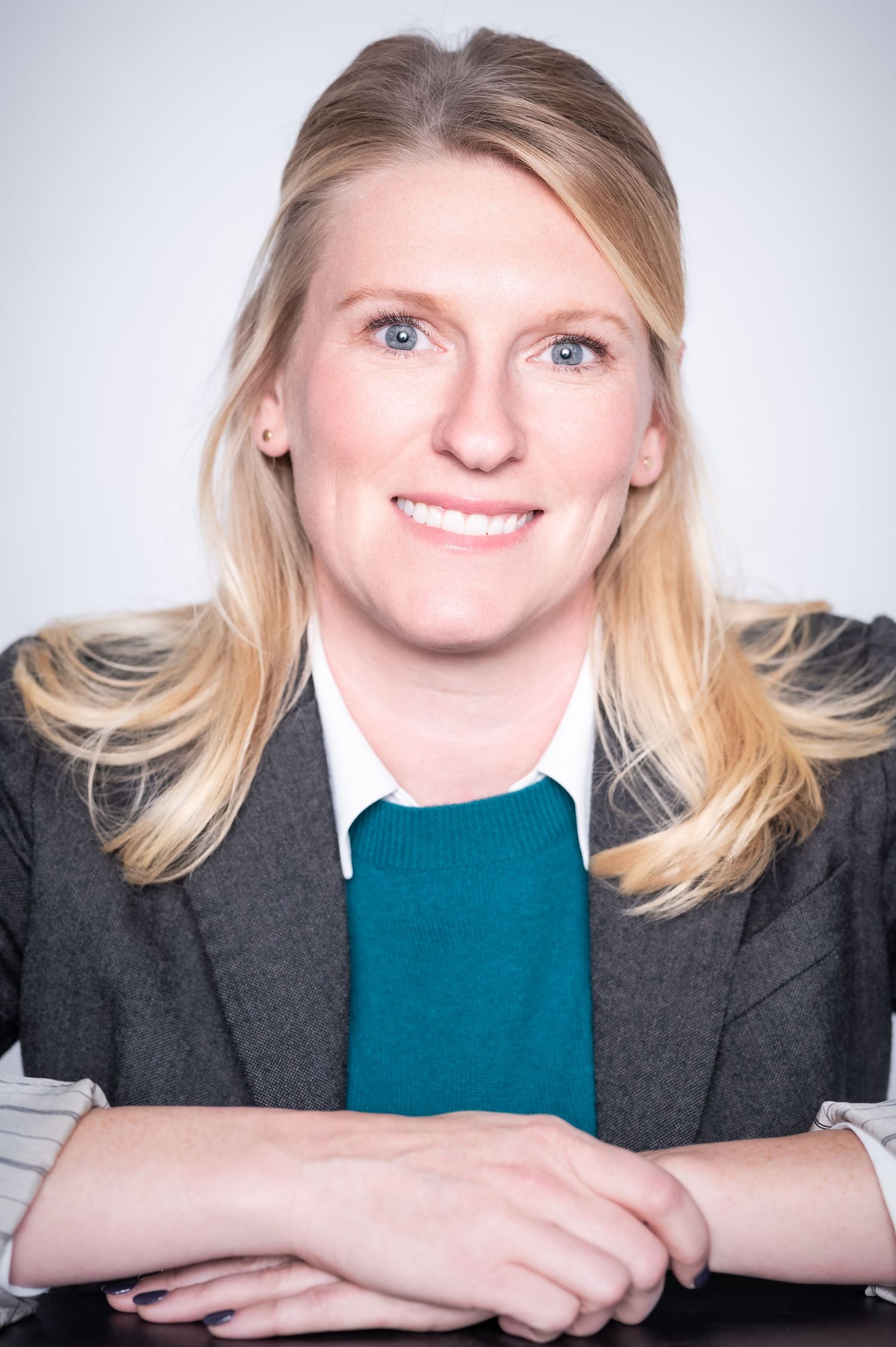 Professional headshot series showing different expressions in a gray blazer and teal top against light background.