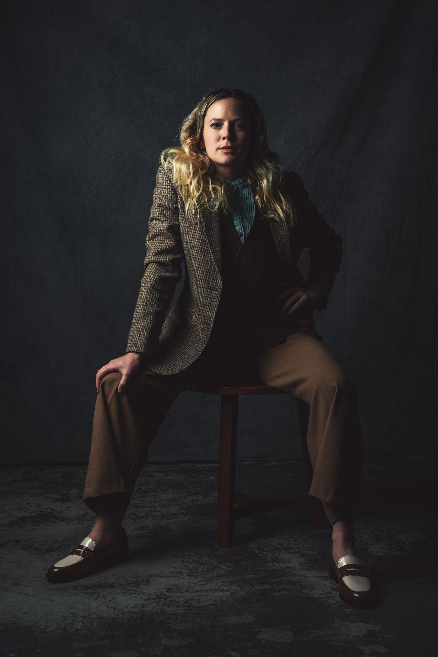 Moody portrait series showing person in vintage suit sitting on wooden chair.