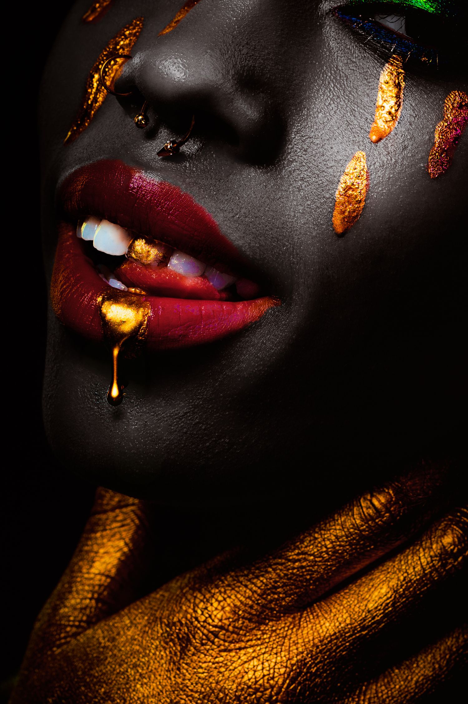 Close-up artistic beauty photo with dark skin, red lips, and glowing gold metallic texture details in dramatic lighting.