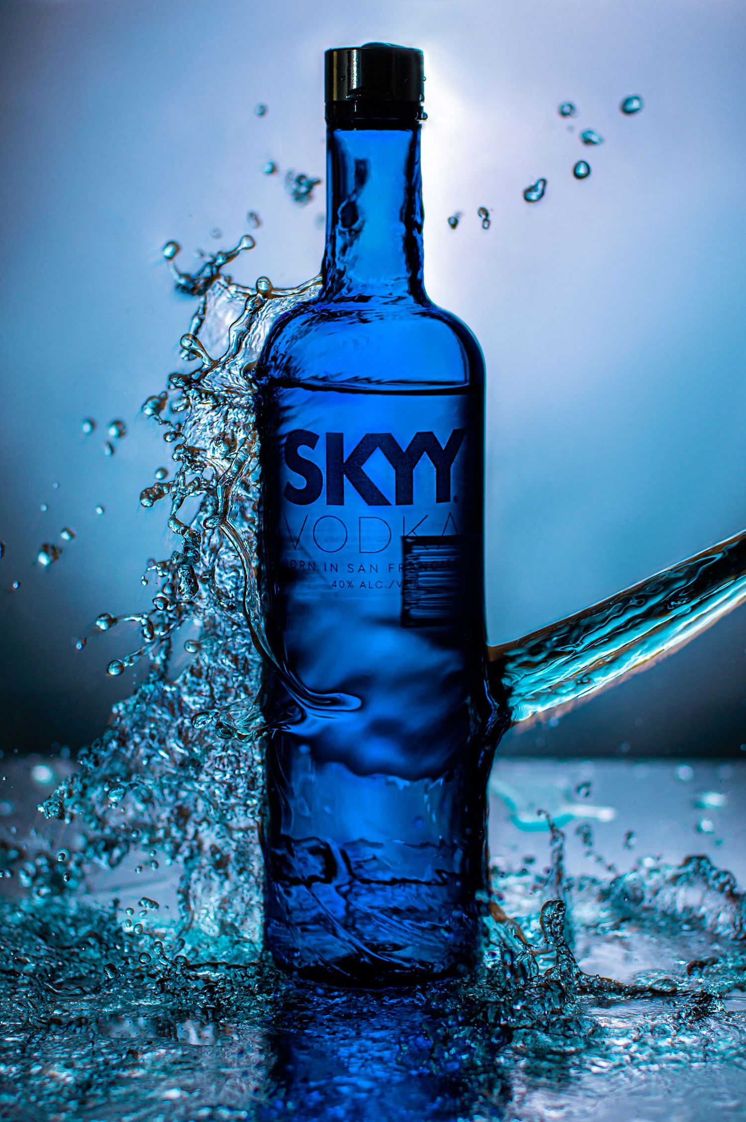 Skyy vodka bottle photographed with dynamic water splashes and blue lighting effects creating a dramatic product shot.