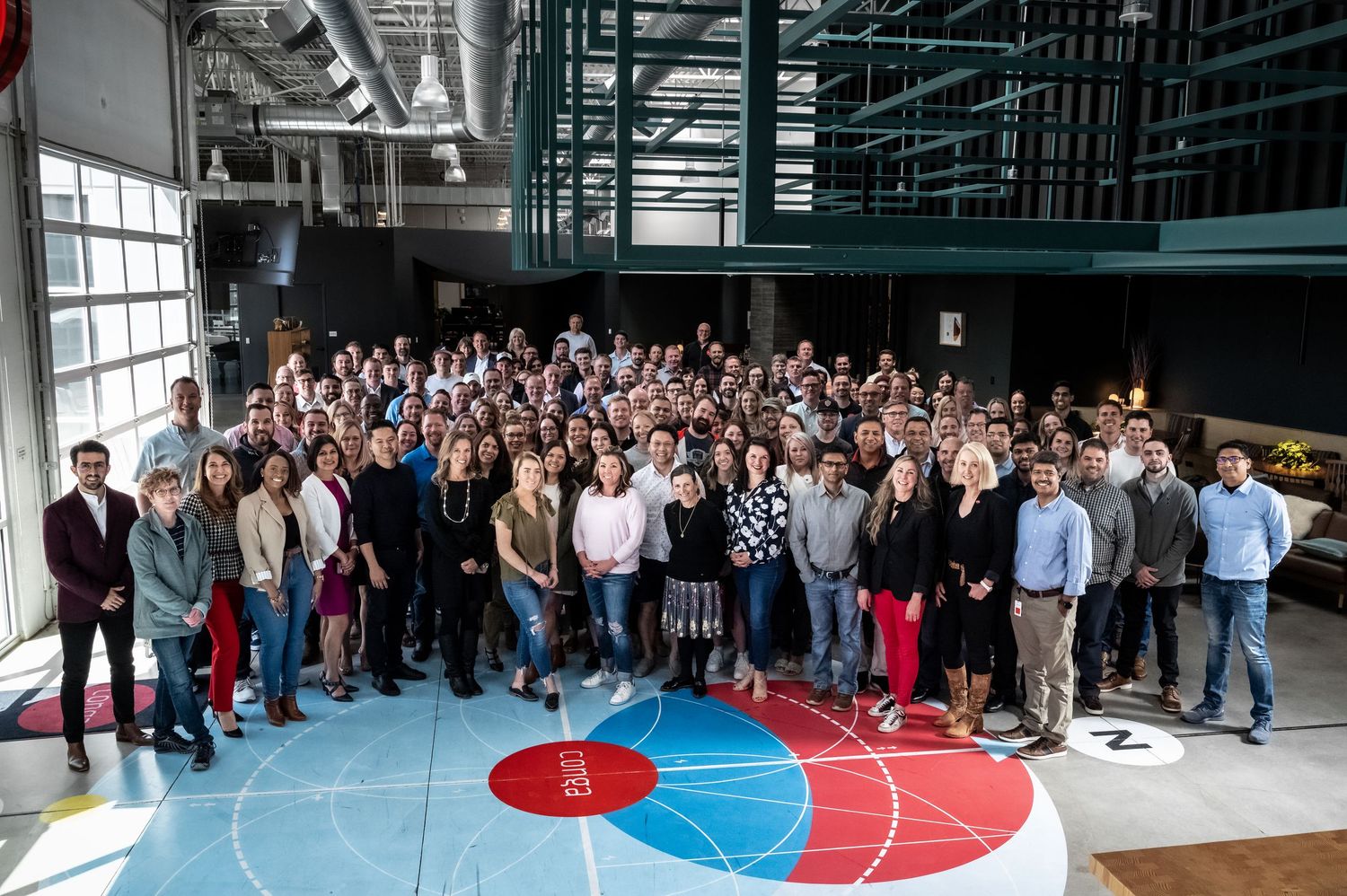 Large group of professionally dressed people gathered for a corporate event in a modern indoor venue.