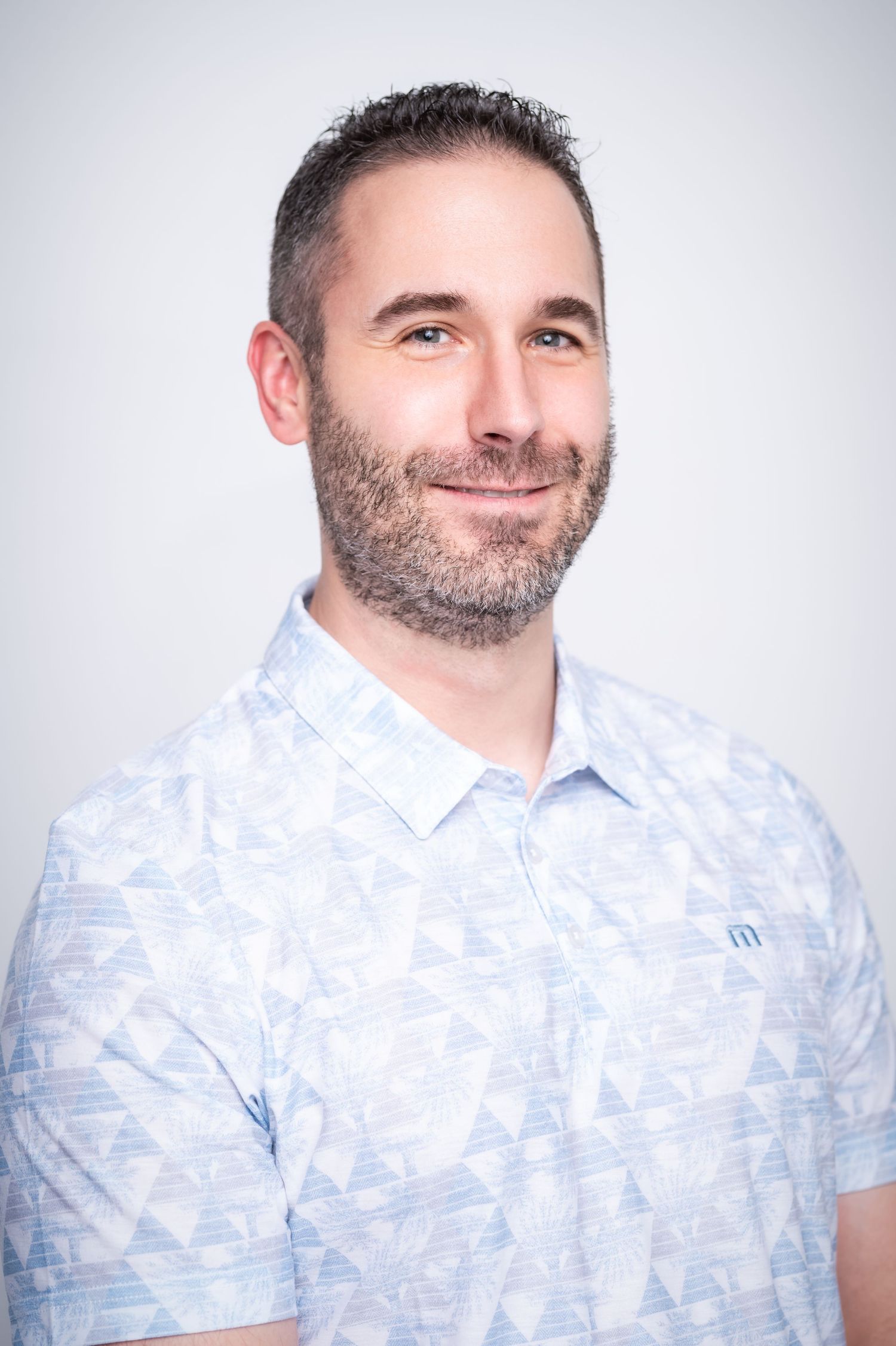 Professional headshots of person in light blue patterned polo shirt against white background.