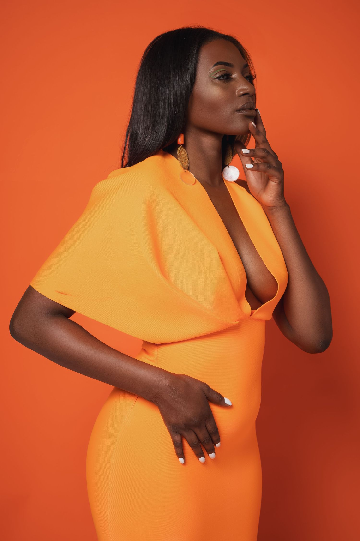 Fashion model in bright orange dress poses elegantly against vibrant orange background in artistic photo series.