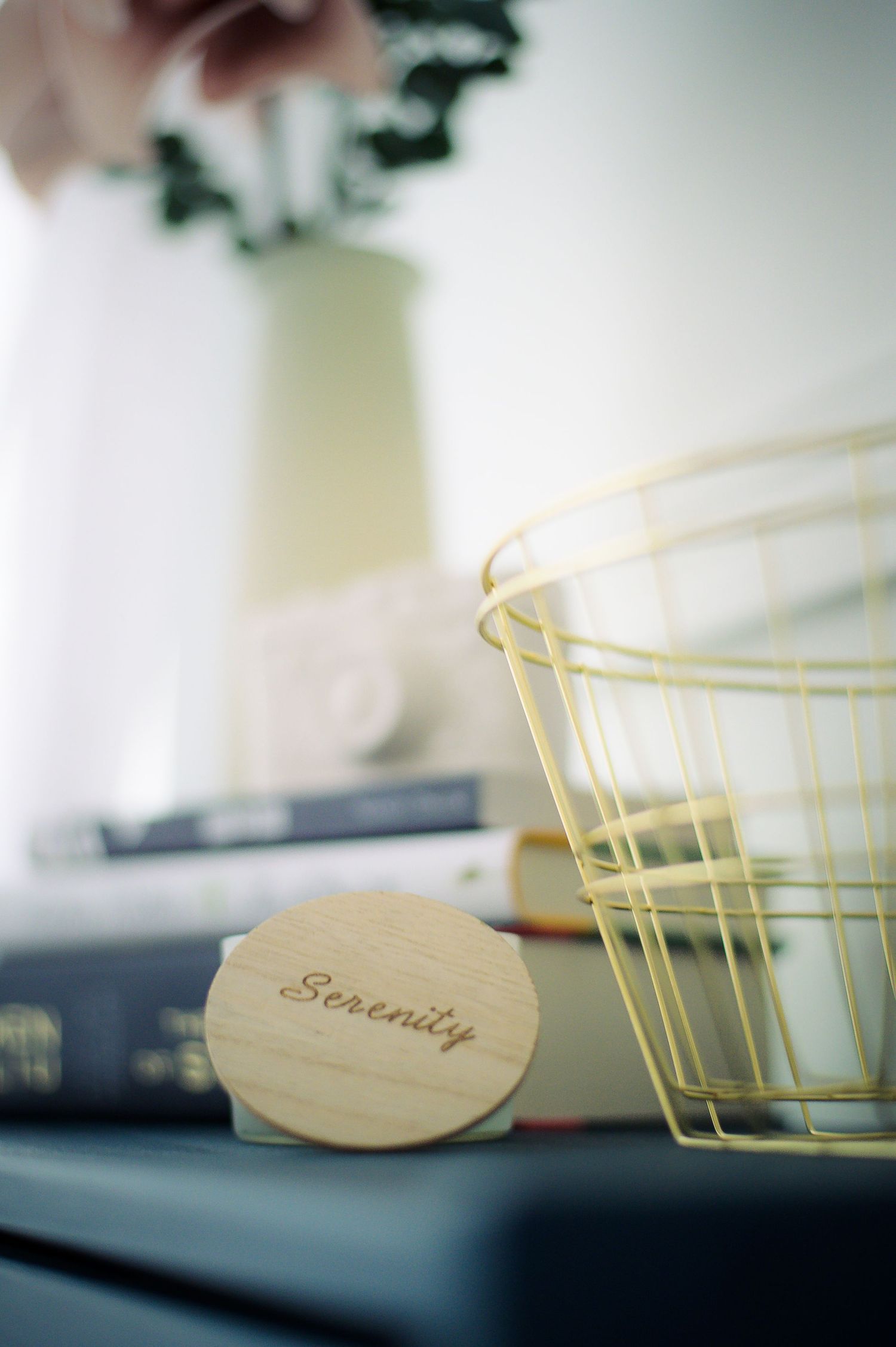 A wooden tag labeled 'Serenity' sits beside stacked books and a yellow wire basket in a soft-focus composition.