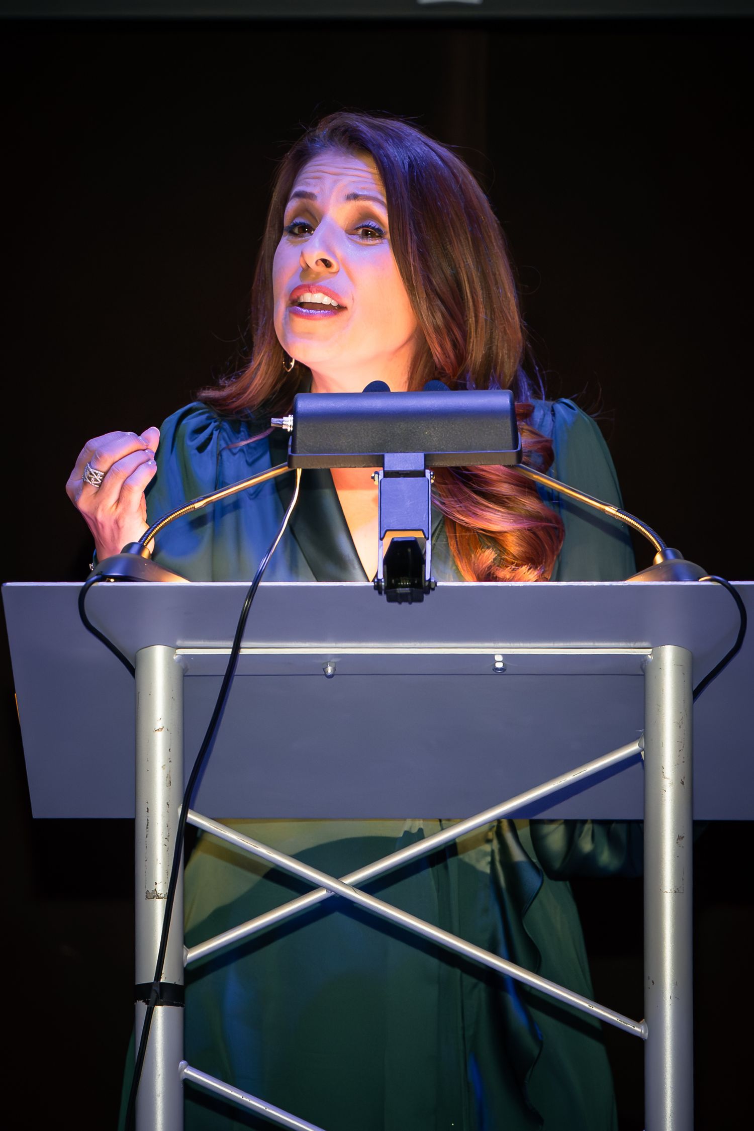 Woman in green dress speaking at a podium with microphone at a formal event.